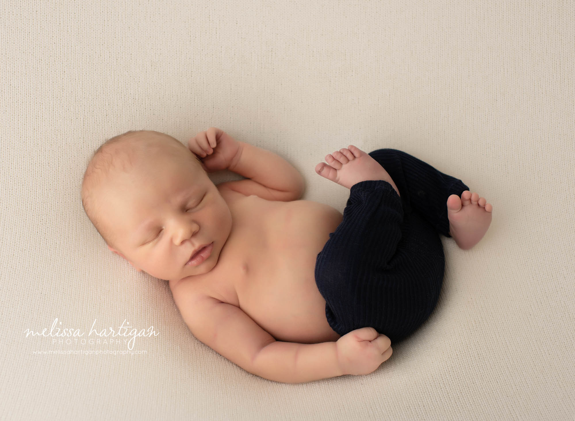 Newborn baby boy posed on back curled up wearing navy blue newborn pants