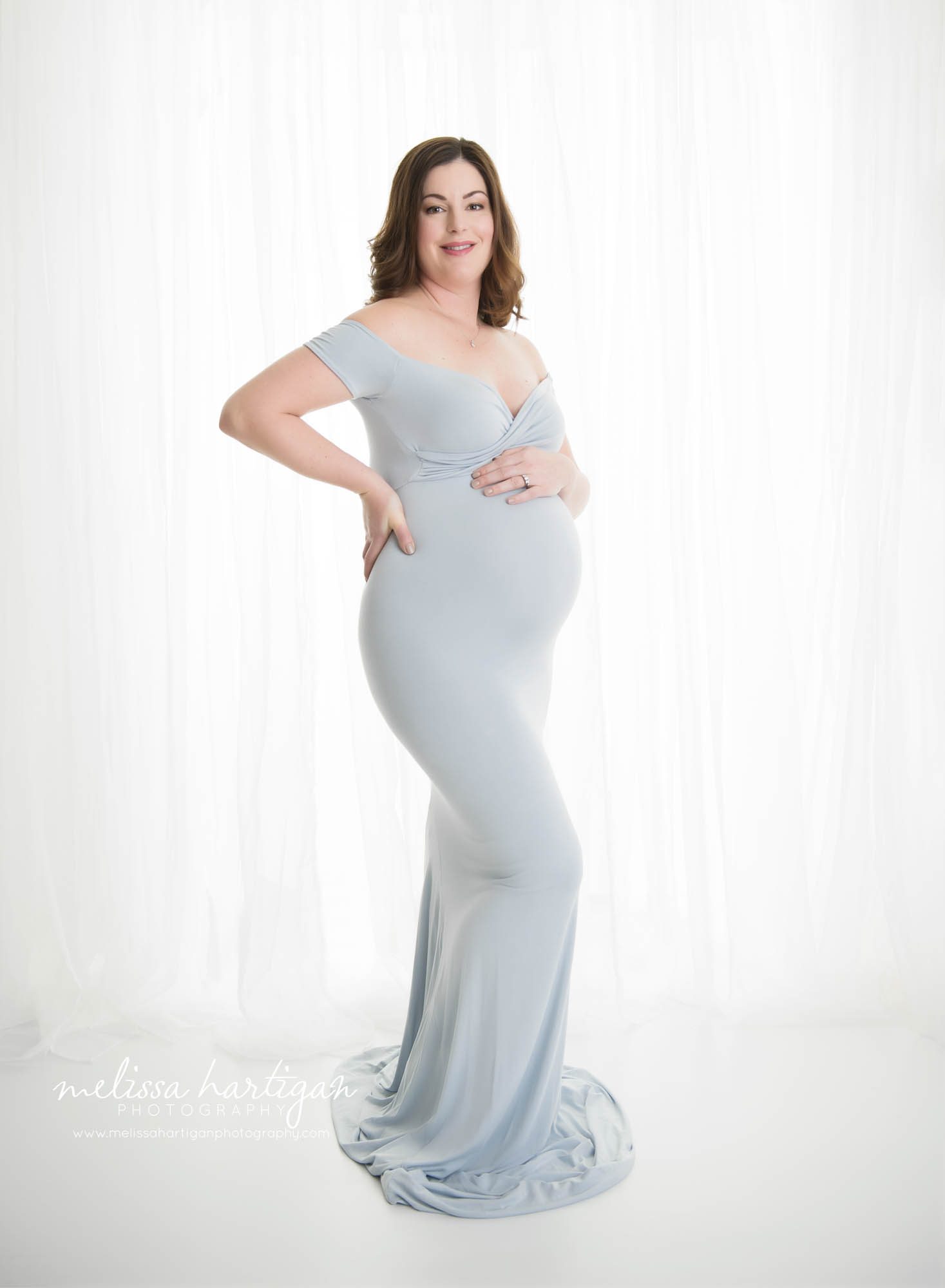 pregnant mom standing maternity pose looking at camera smiling one hand on baby bump one hand on back Tolland Maternity Photographer