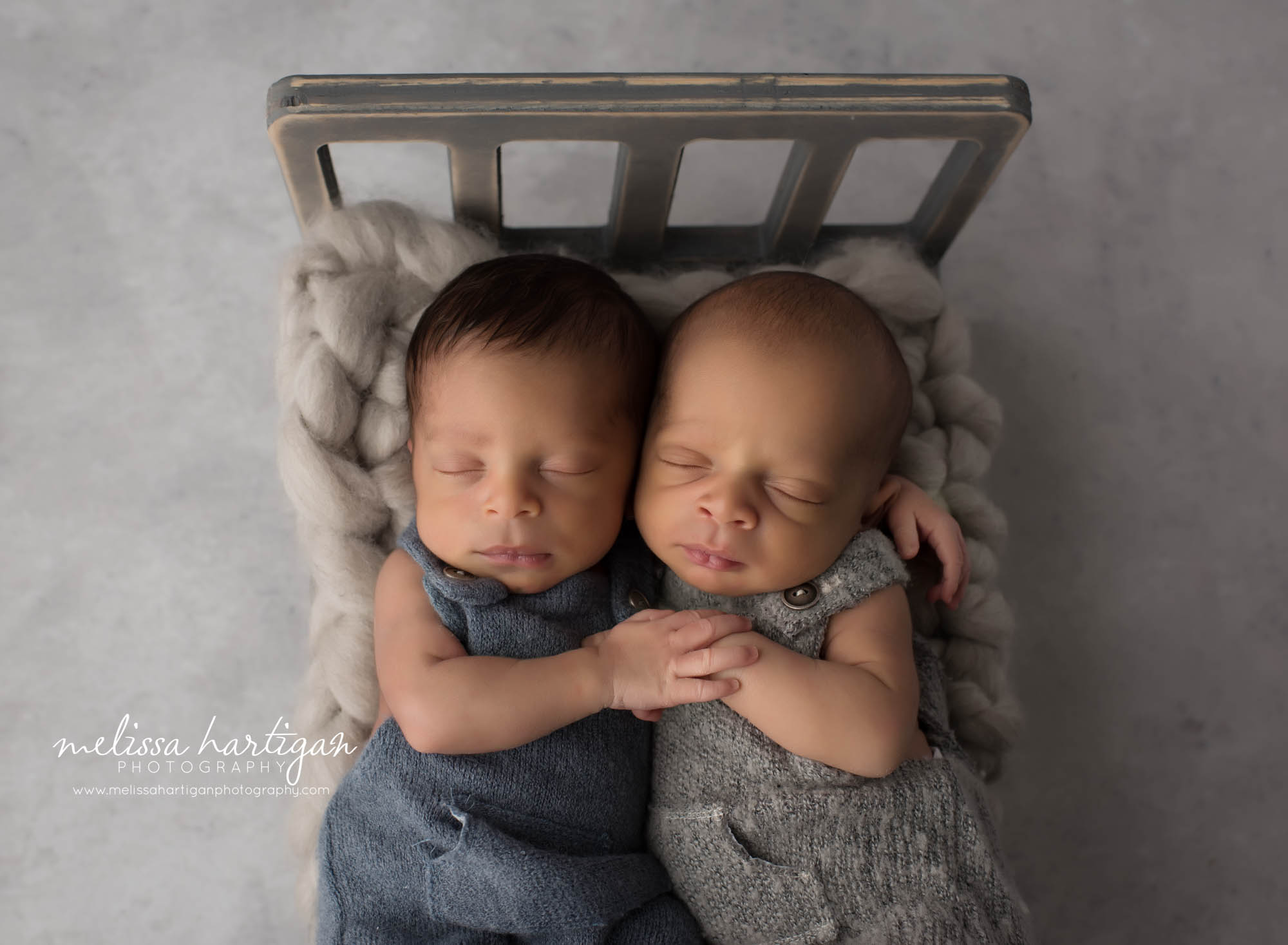 newborn twin boys posed on wooden bed prop wearing blue and gray newborn outfits CT newborn Photographer