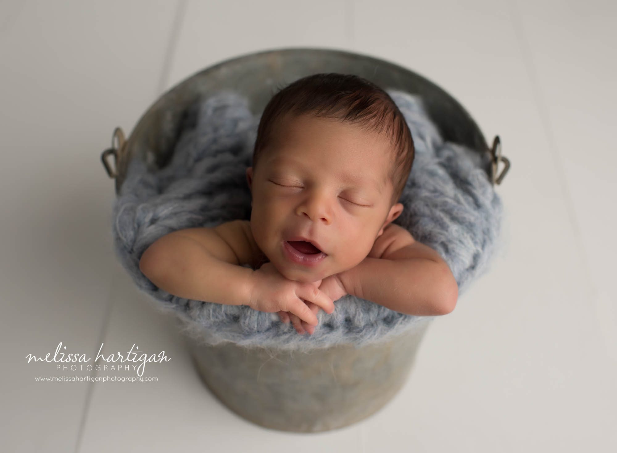 Newborn baby boy posed in metal bucket with blue knitted layer
