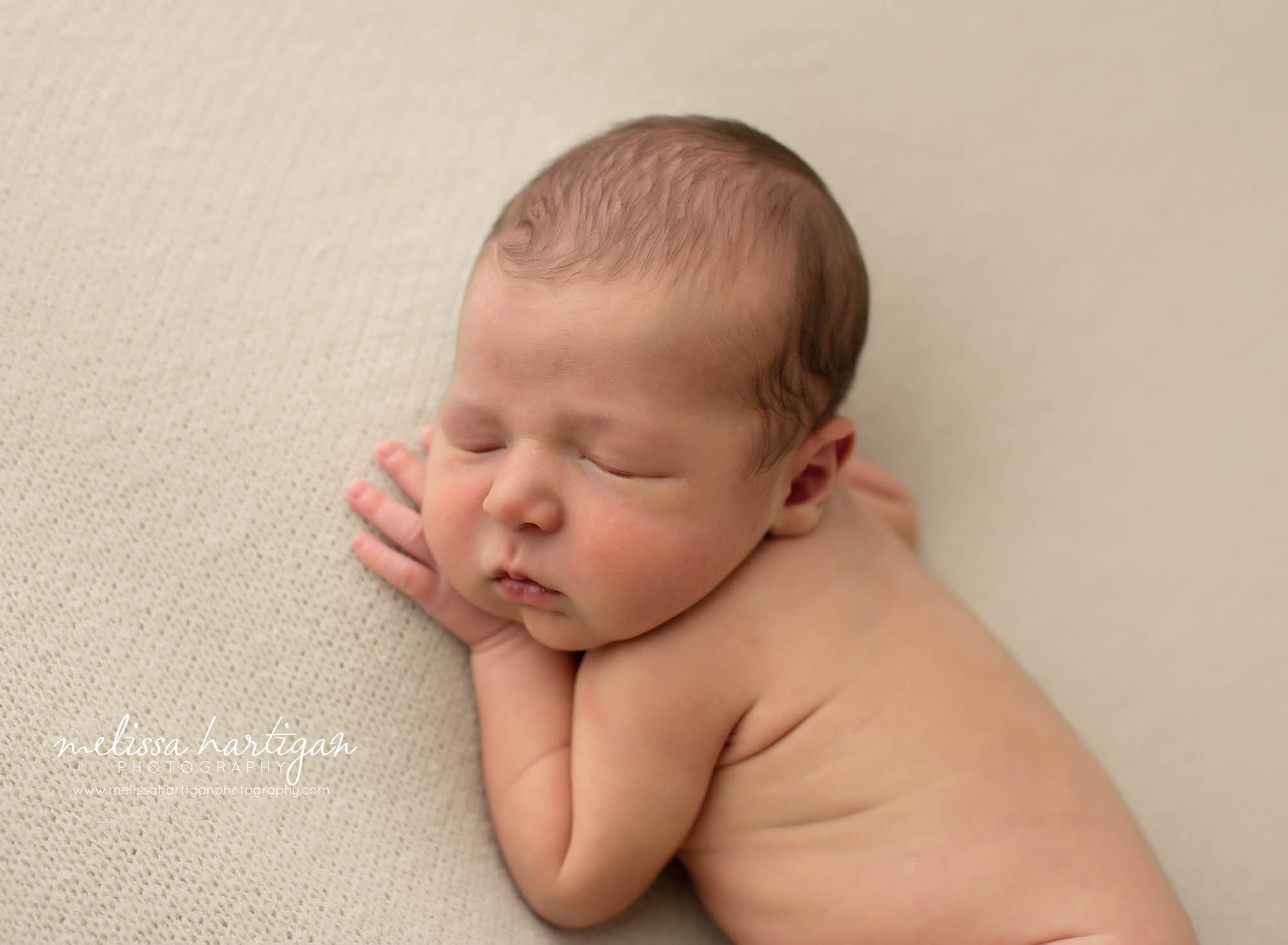 Newborn baby boy posed on side with hand under chin