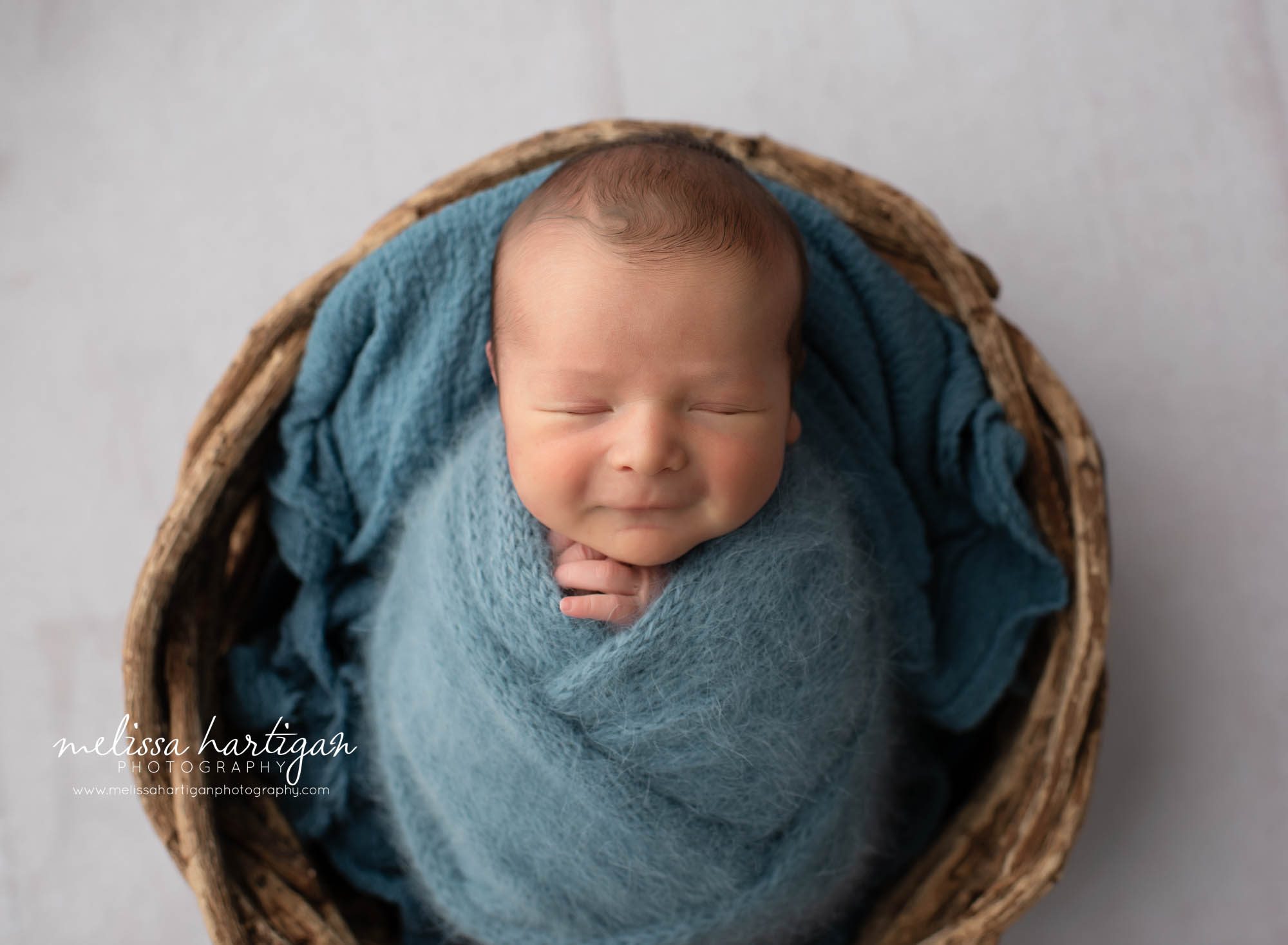 newborn baby boy wrapped in teal blue knitted wrap posed in wicker basket Connecticut newborn photographer