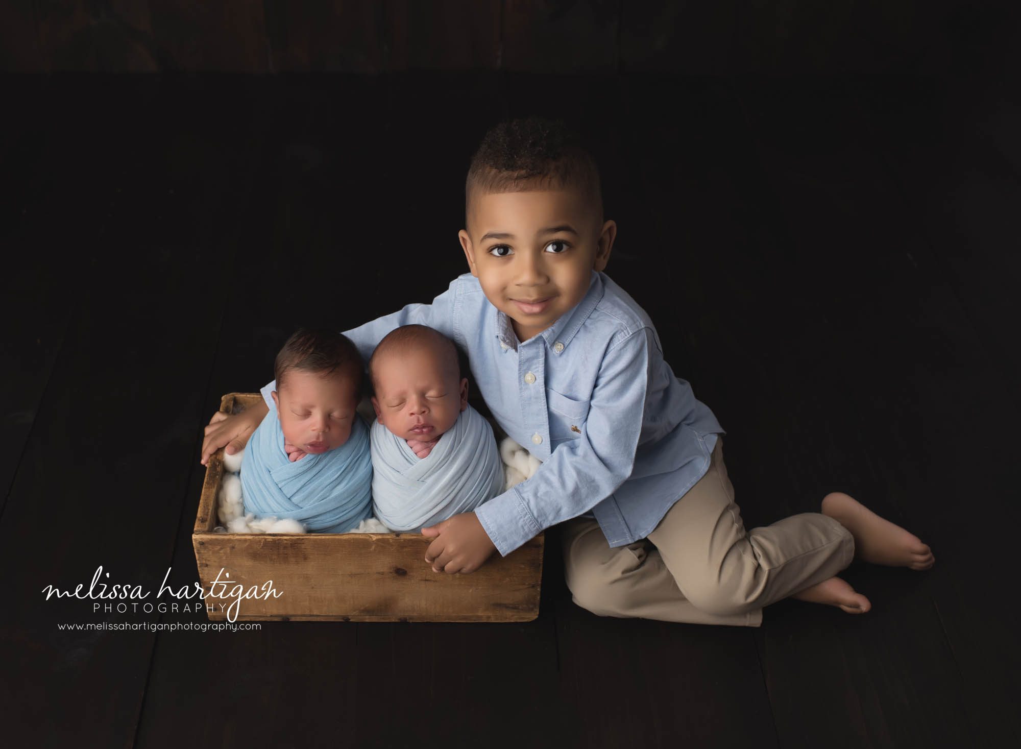 big brother sitting next to sooden crate with twin baby boys brothers wrapped up sibling photo