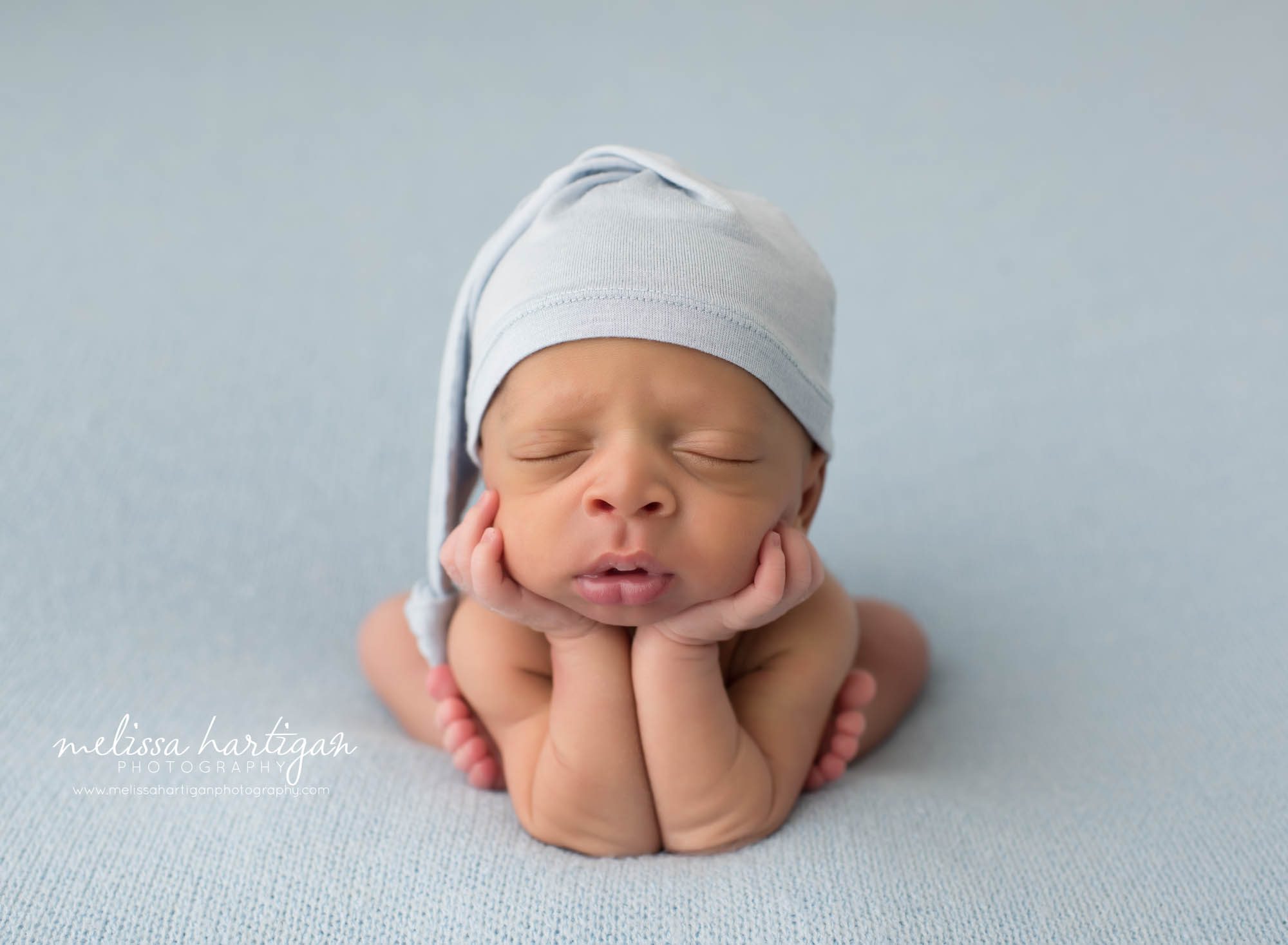 Newborn baby boy posed in froggy pose light blue sleepy cap