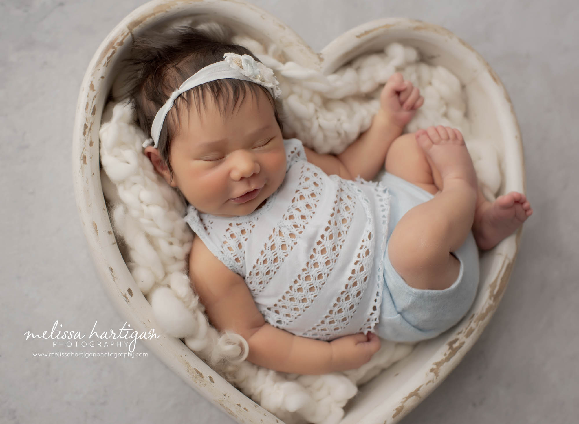newborn baby girl posed in wooden heart prop with light blue newborn outfit and matching headband