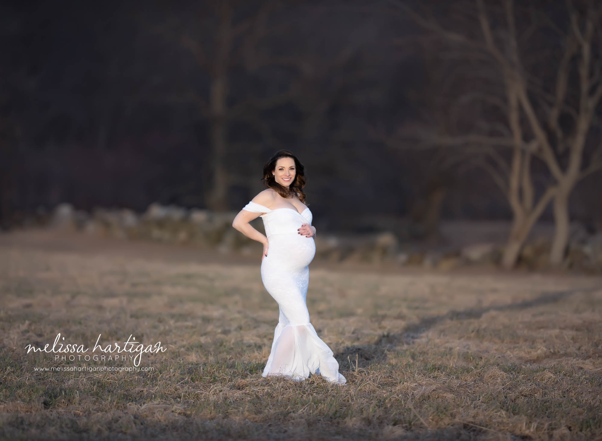 expectant mom holding baby bump smiling at camera outside maternity photography photos