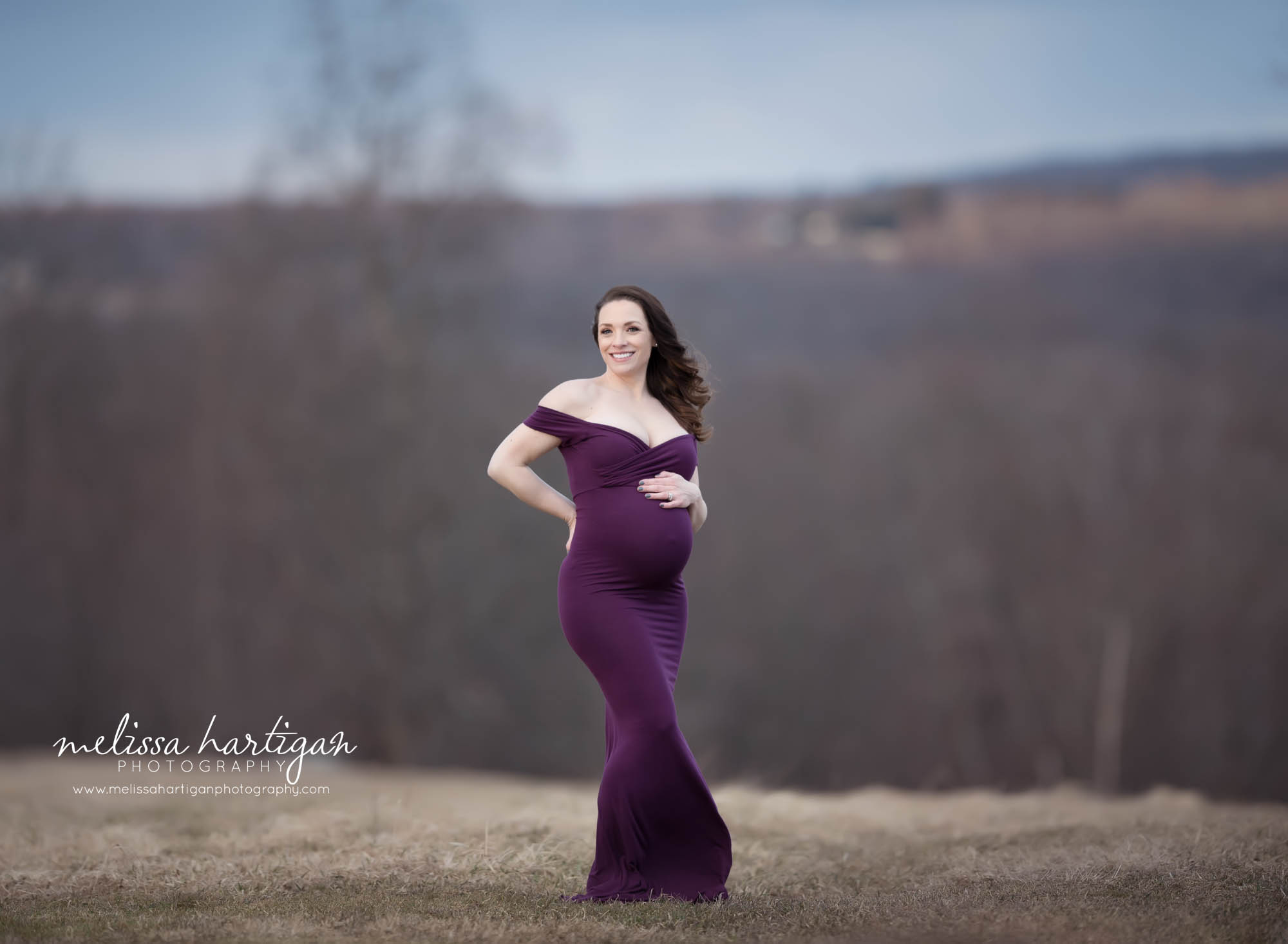 pregnant mom standing maternity pose outside wearing long purple form fitting maternity gown