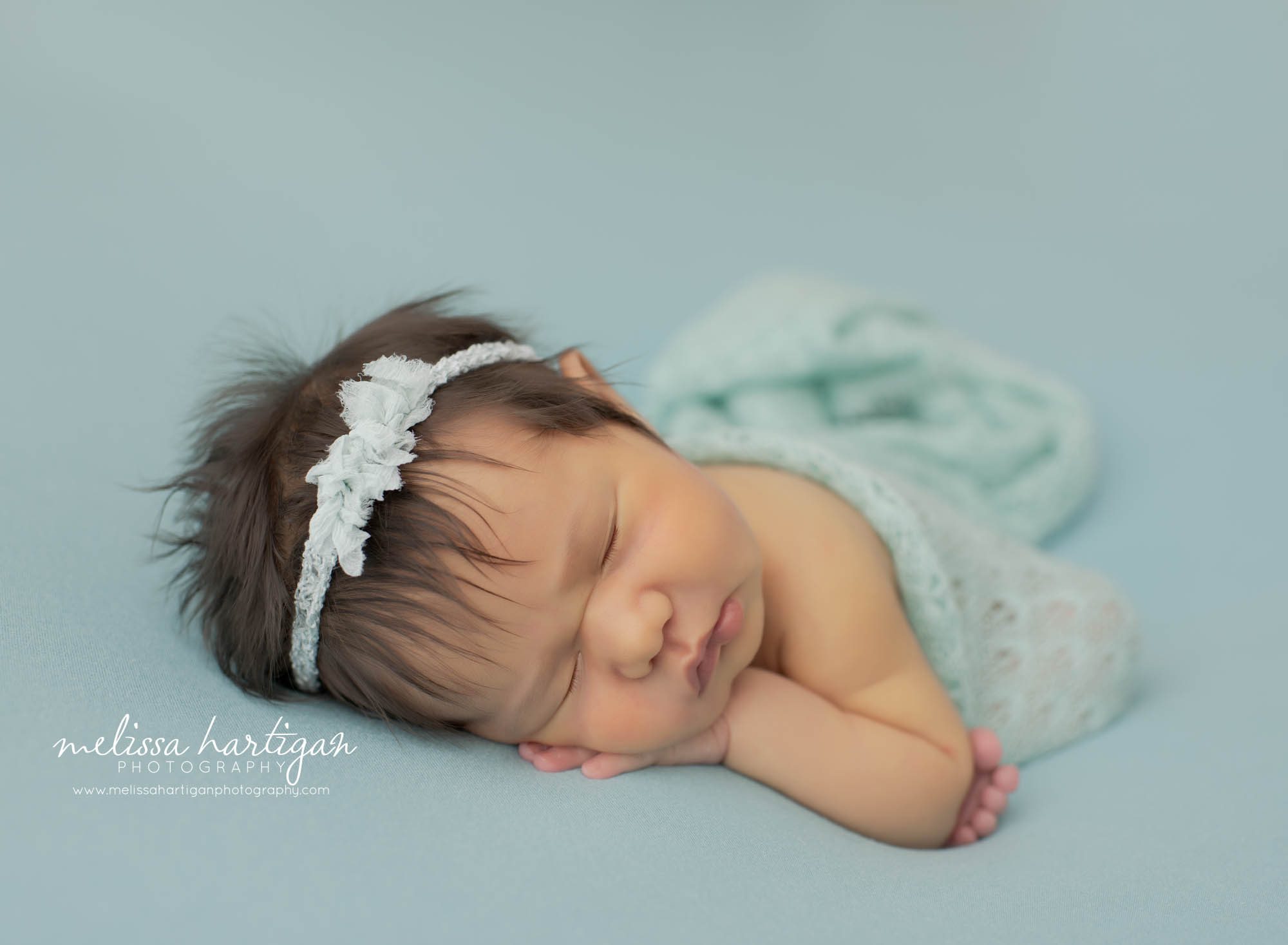 newborn baby girl posed on side sleeping wearing light sea green bow headband