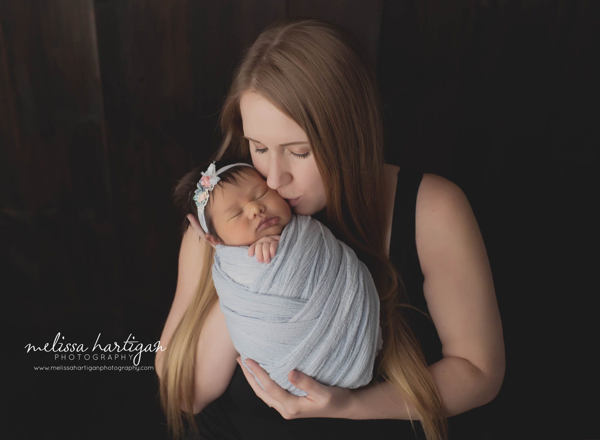 mom holding newborn baby girl giving baby kiss in newborn studio photography session