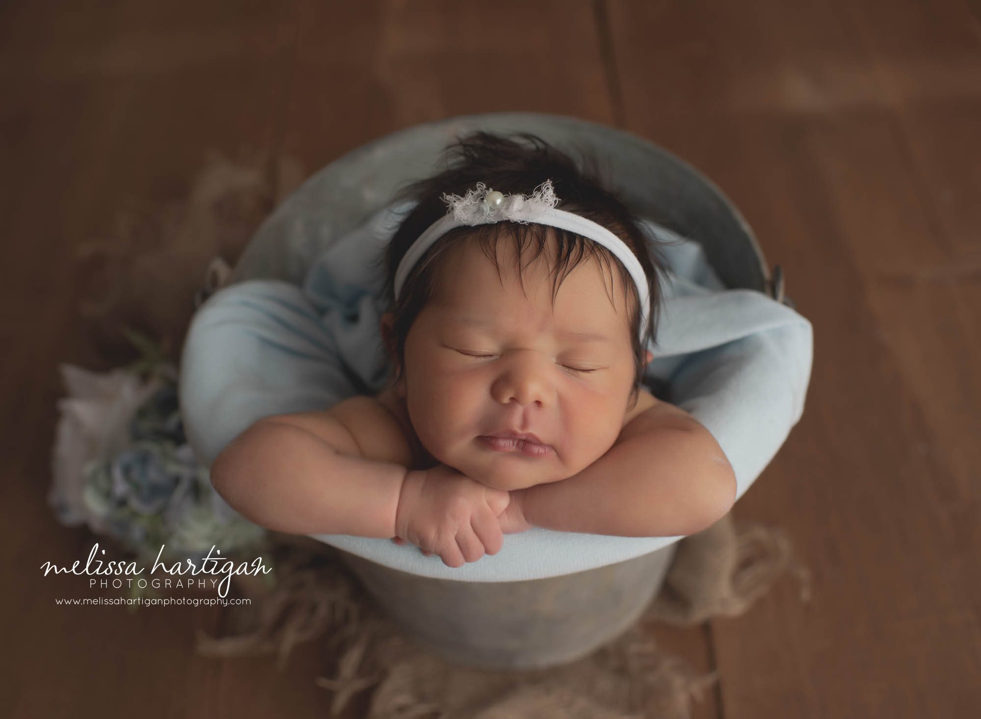 Newborn baby girl pose din metal bucket with light blue wrap and light blue headband tieback with pearls and floral elements
