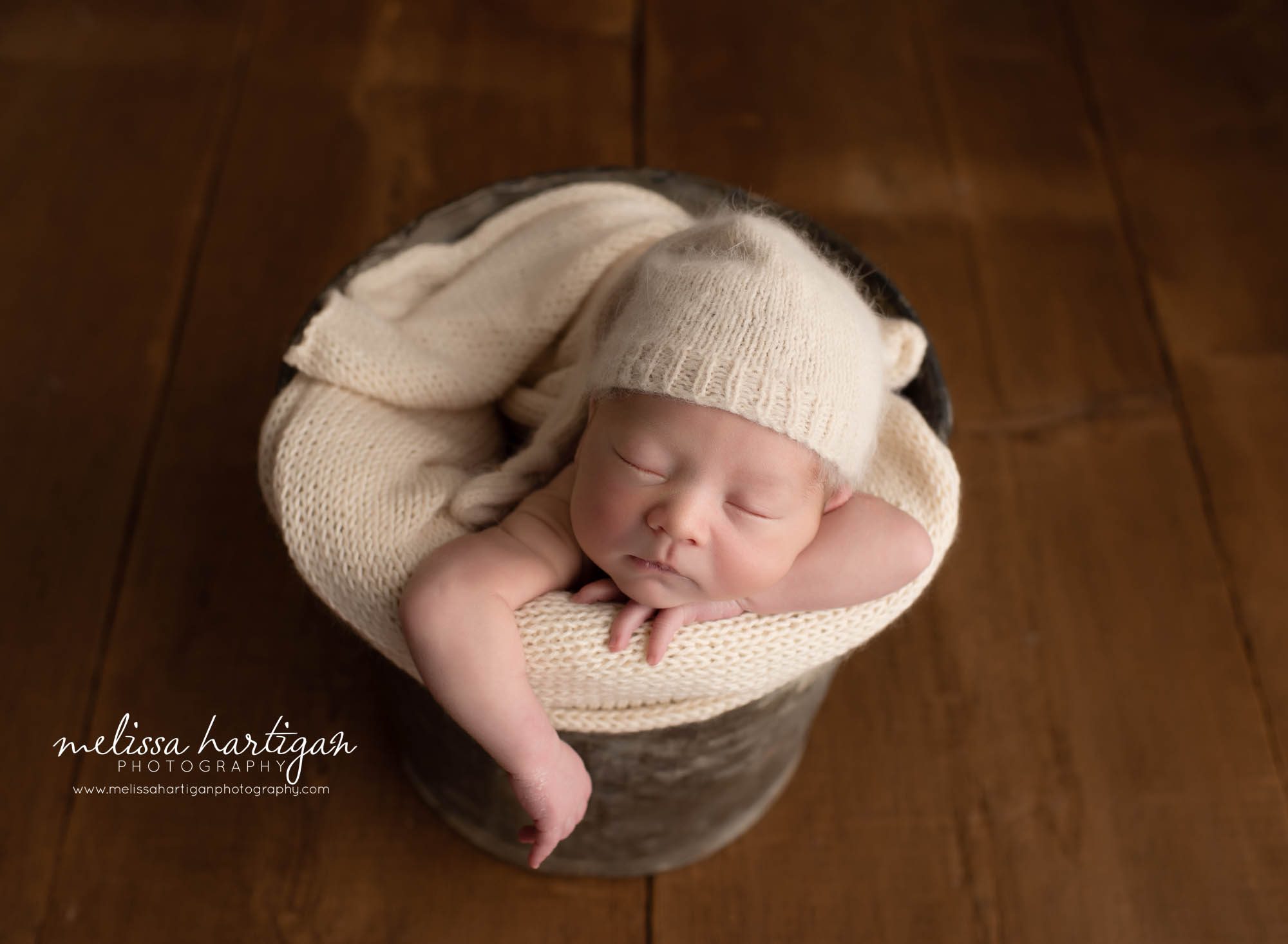 newborn baby boy posed in bucket with cream knitted wrap and sleepy cap