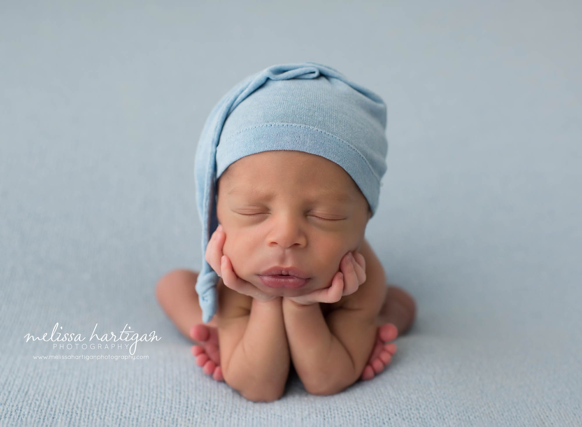 newborn baby boy posed froggy pose blue sleepy cap