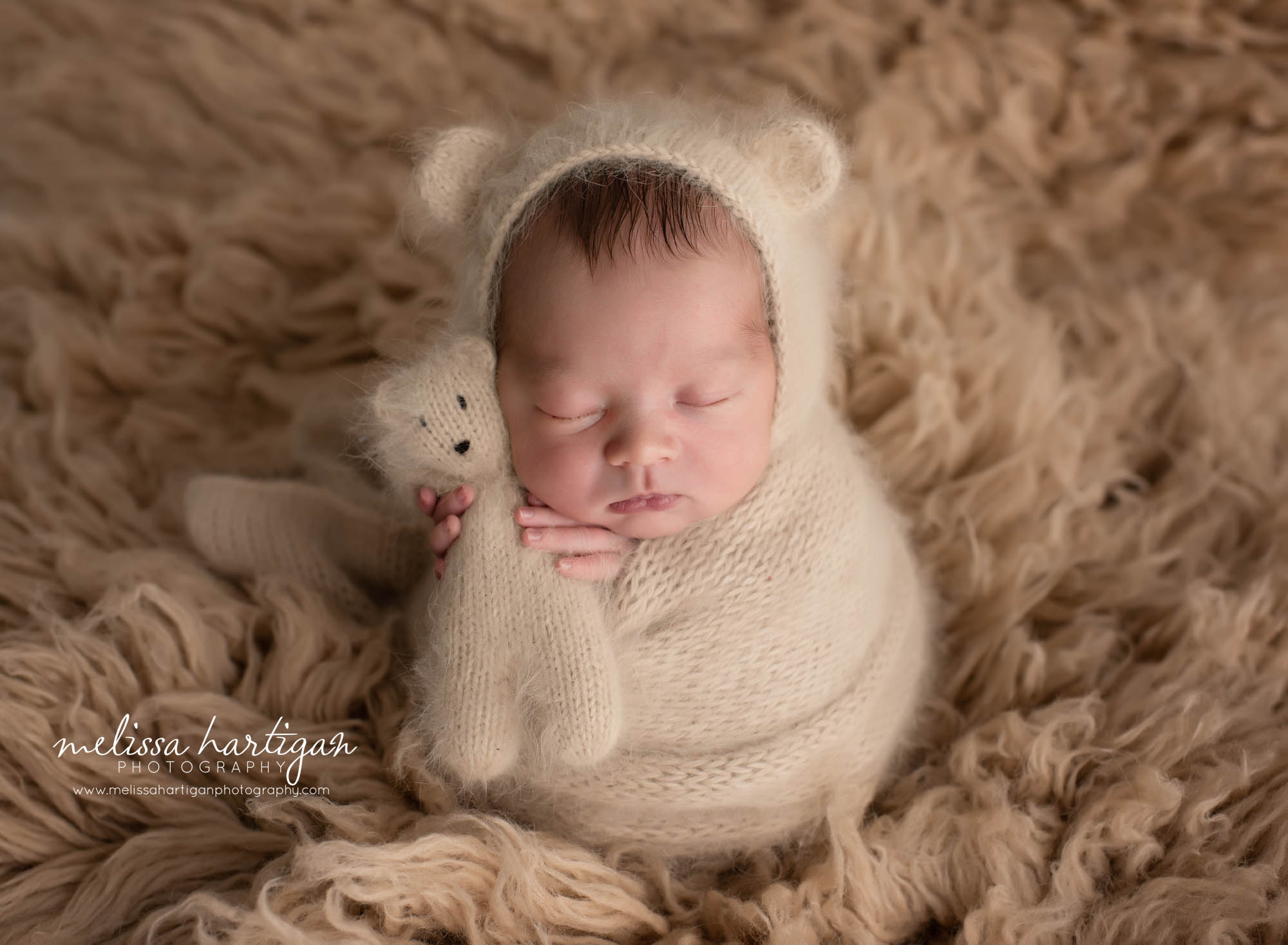 Newborn Baby boy posed in caramel color knitted wrap with matching bear bonnet and teddy bear flokati