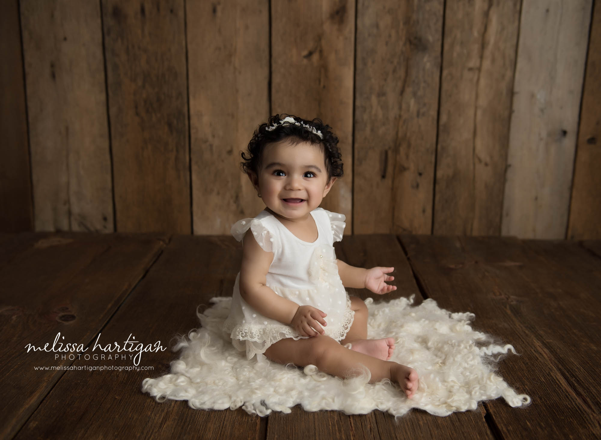 Smiling baby girl sitting on fluffy layer on wooden boards baby photographer CT