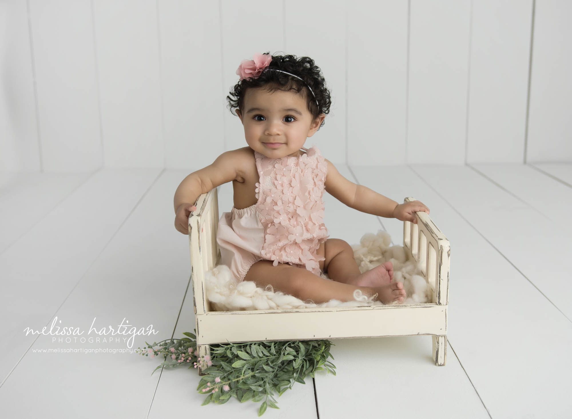 baby girl sitting on wooden bed prop in studio photography session capturing sitting up baby milestone