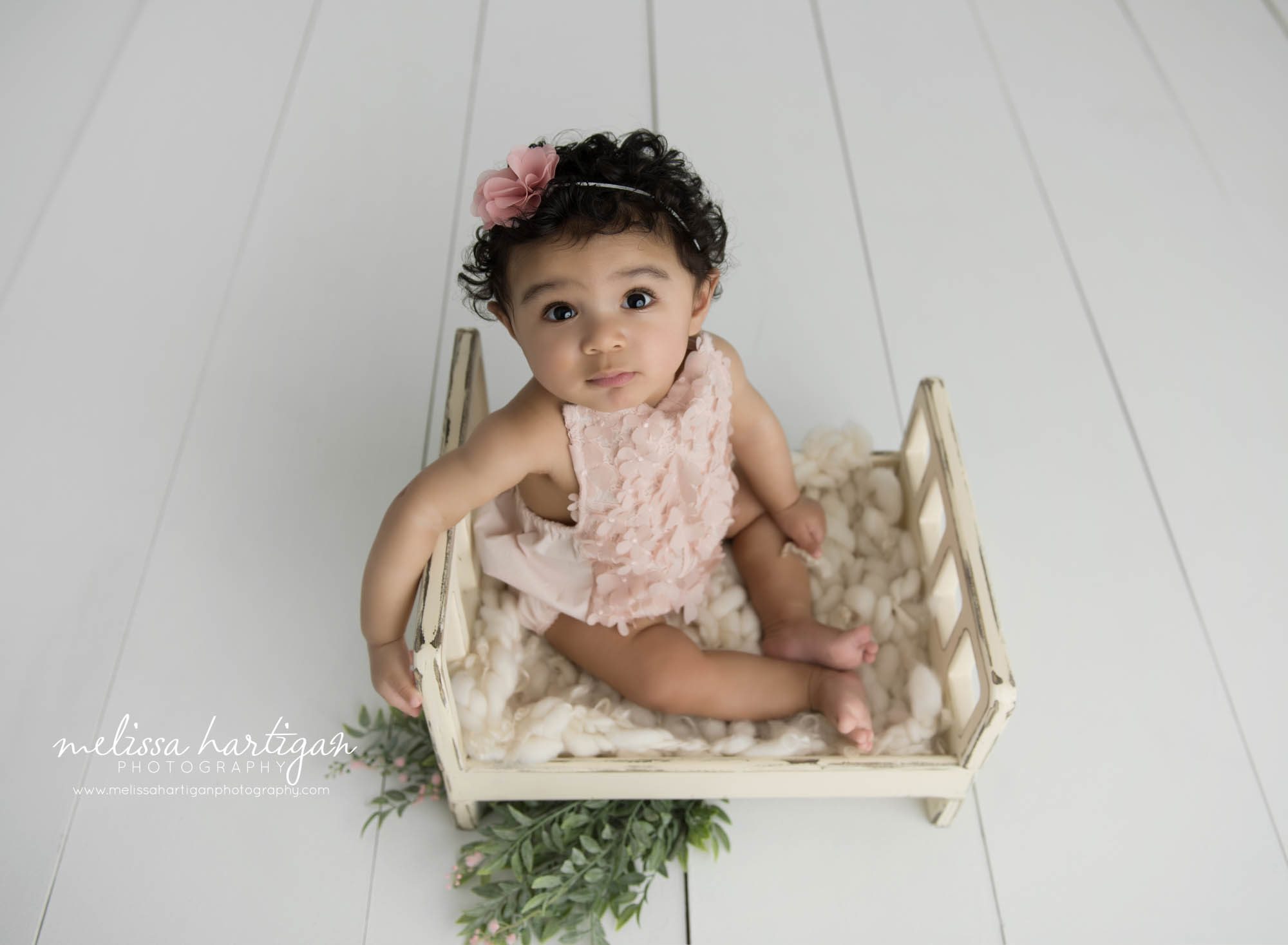 baby girl sitting on wooden bed prop looking up at camera