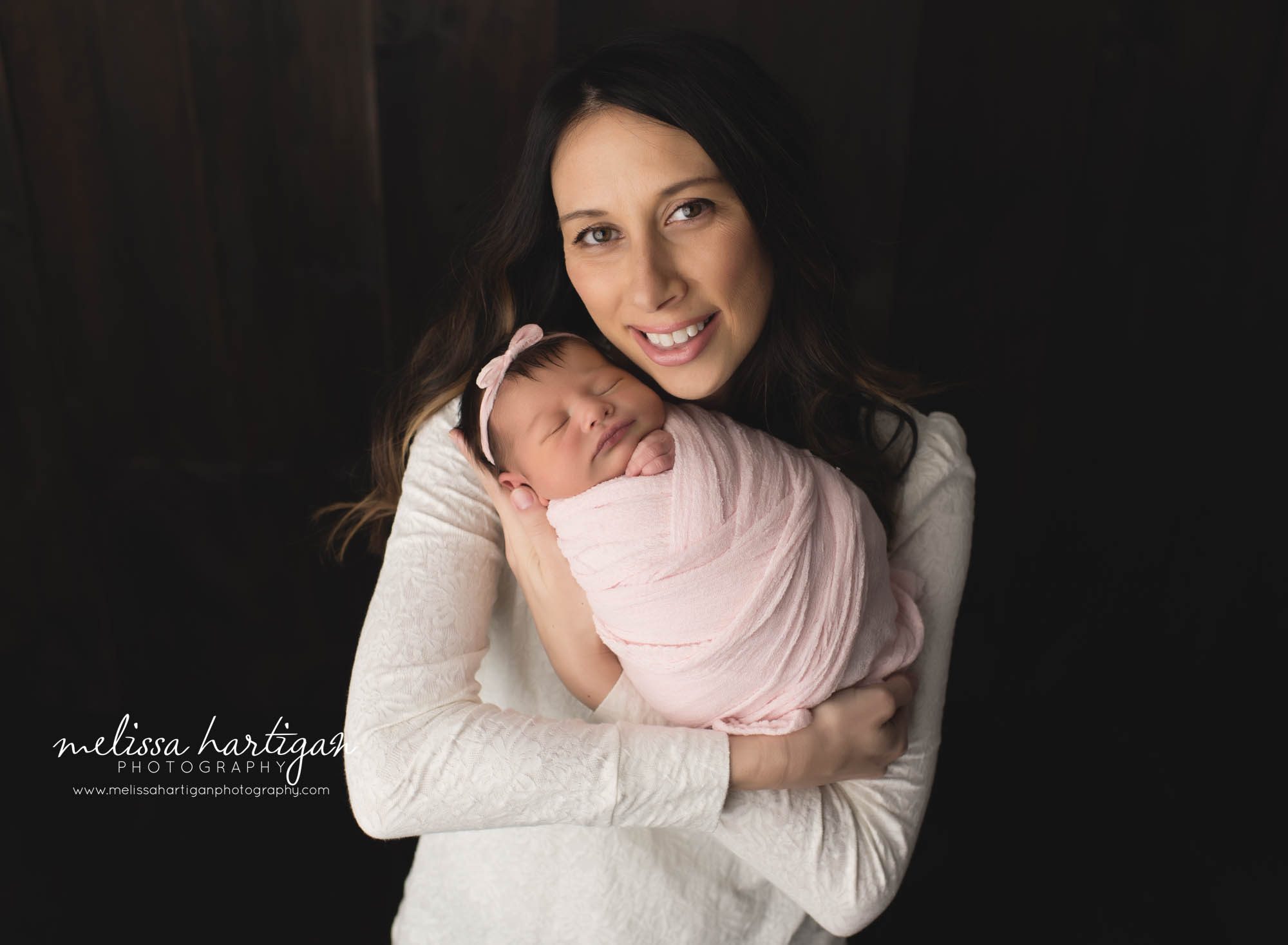 mom holding newborn baby girl wrapped in pink wrap with pink bow headband in CT studio newborn photography parent pose
