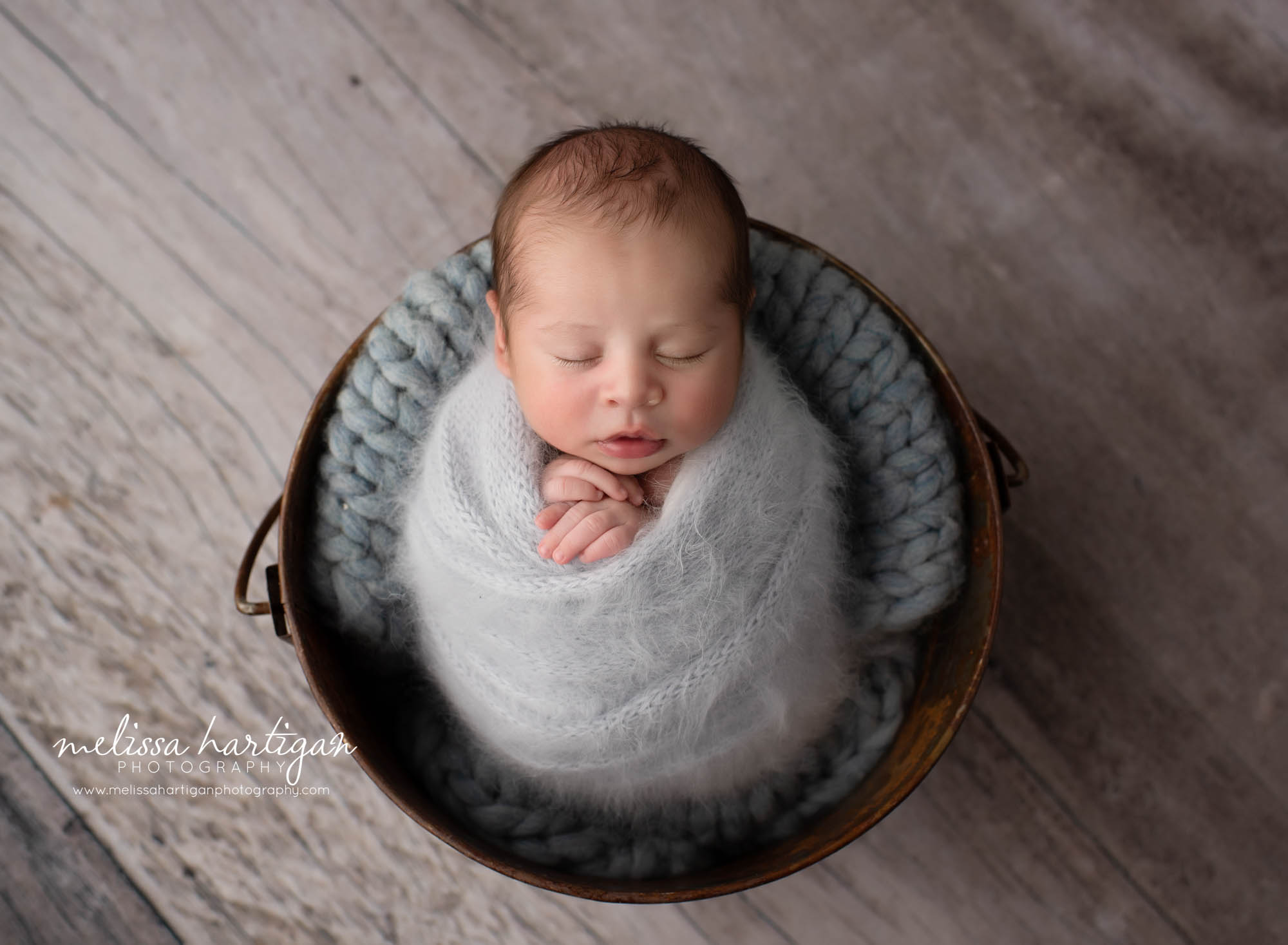 Newborn baby boy swaddled in knitted gray wrap posed in bucket