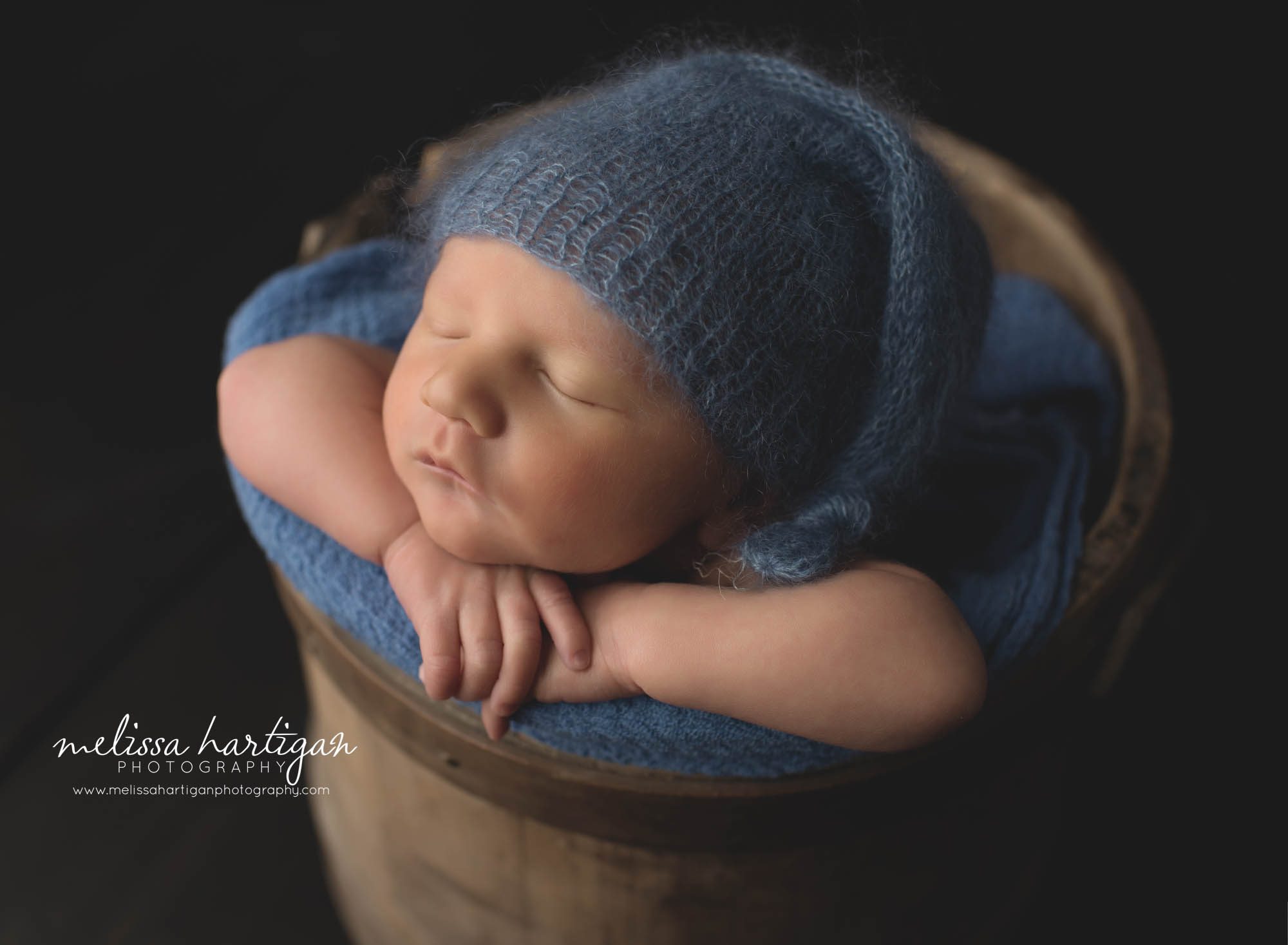 baby boy posed in wooden bucket with blue knitted sleepy cap