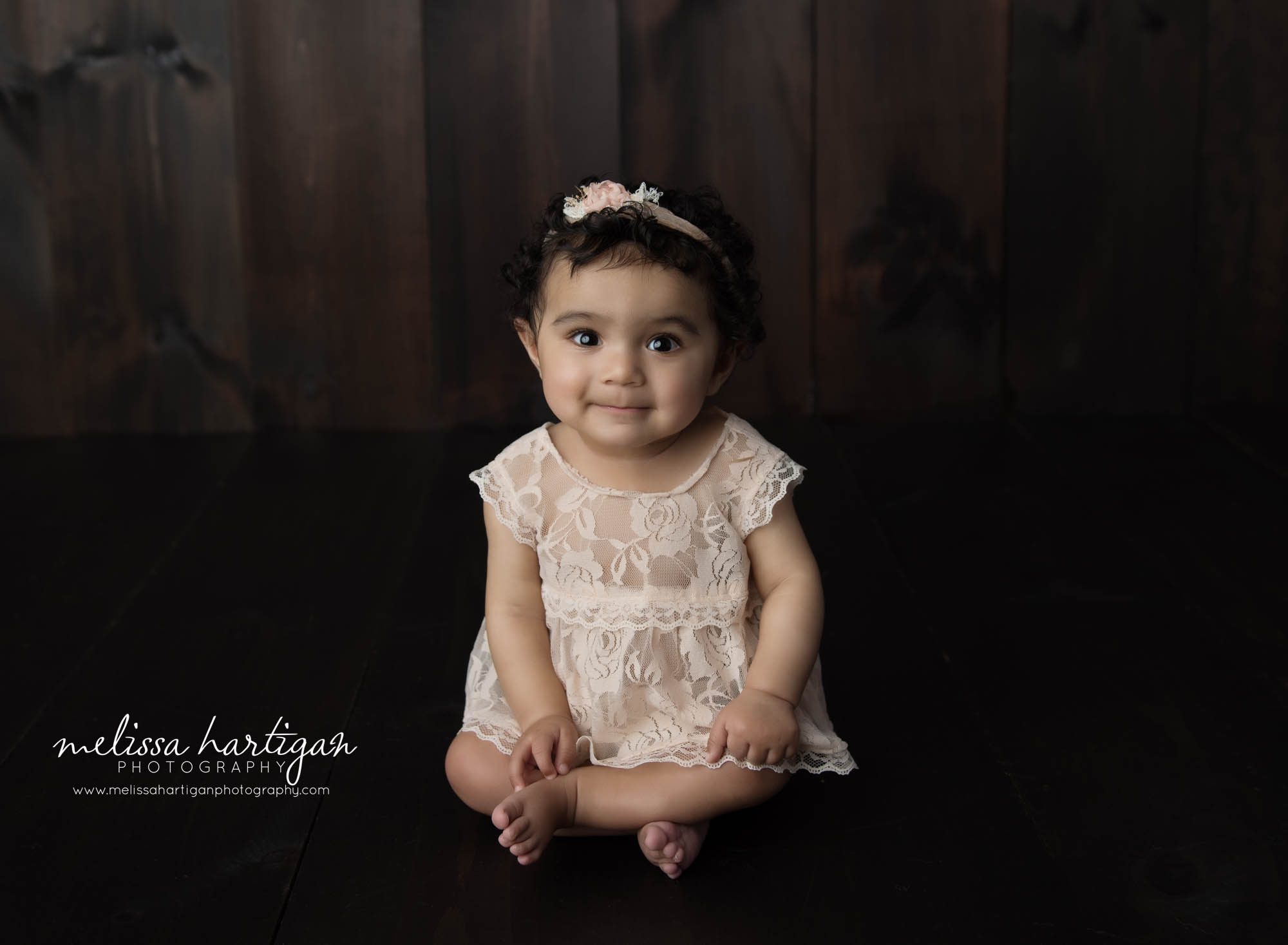 baby girl sitting cross legged on wooden boards in studio photo session