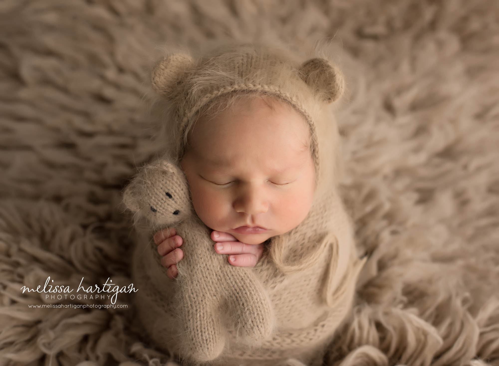 Newborn baby boy wrapped in caramel colored knitted werap with matching knitted bear bonnet and teddy bear