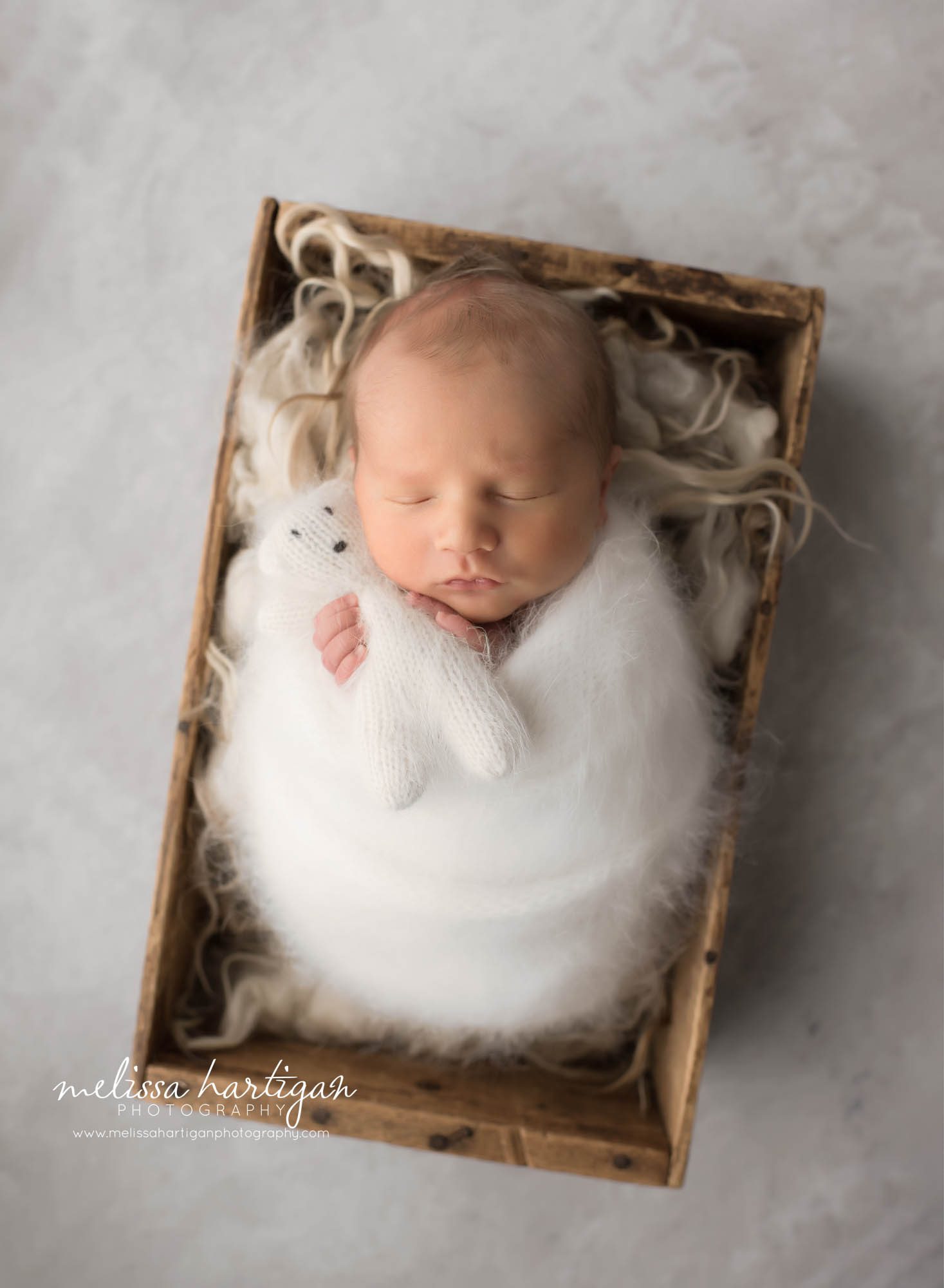 Baby boy wrapped in white wrap with matching knitted teddy bear