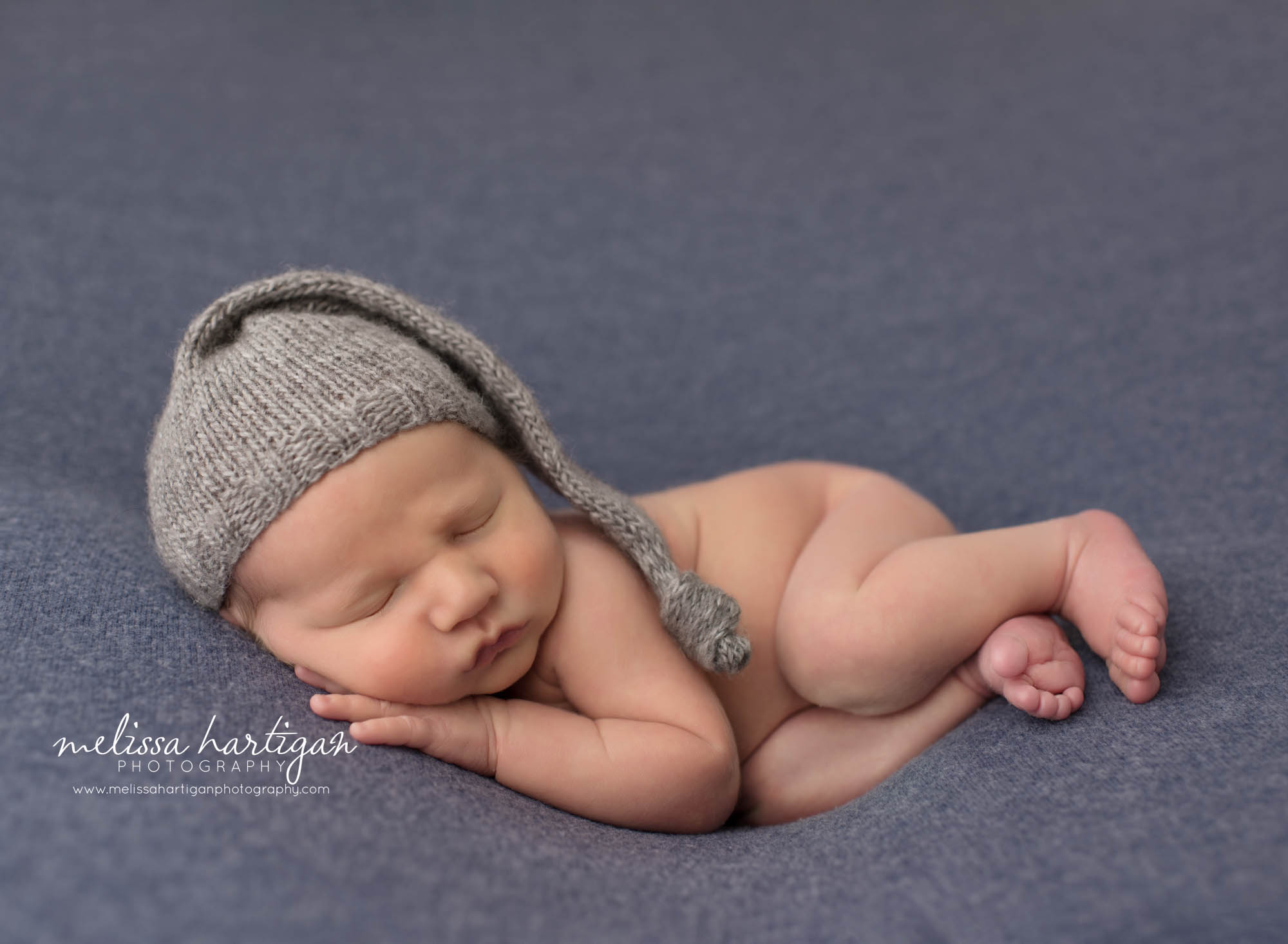 Newborn baby boy posed on side with gray sleepy cap