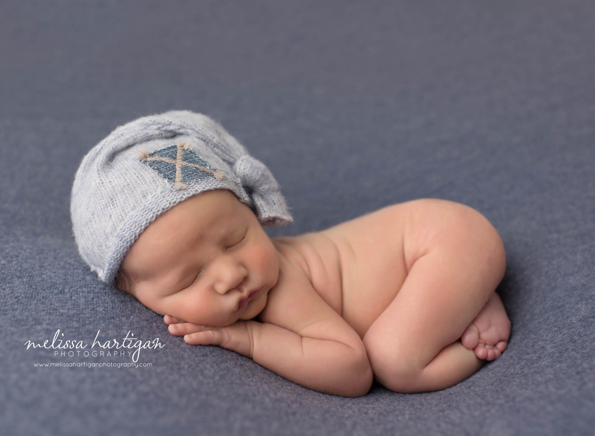 Newborn baby boy posed on tummy bump up with blue sleepy cap