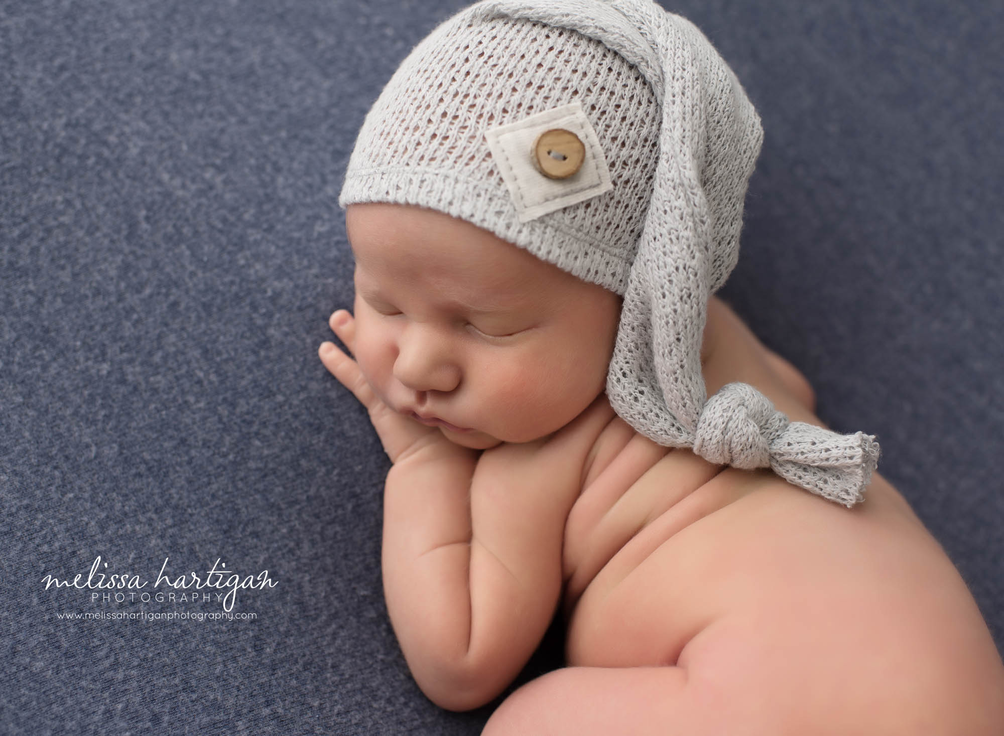 Newborn baby boy posed on side with gray sleepy cap