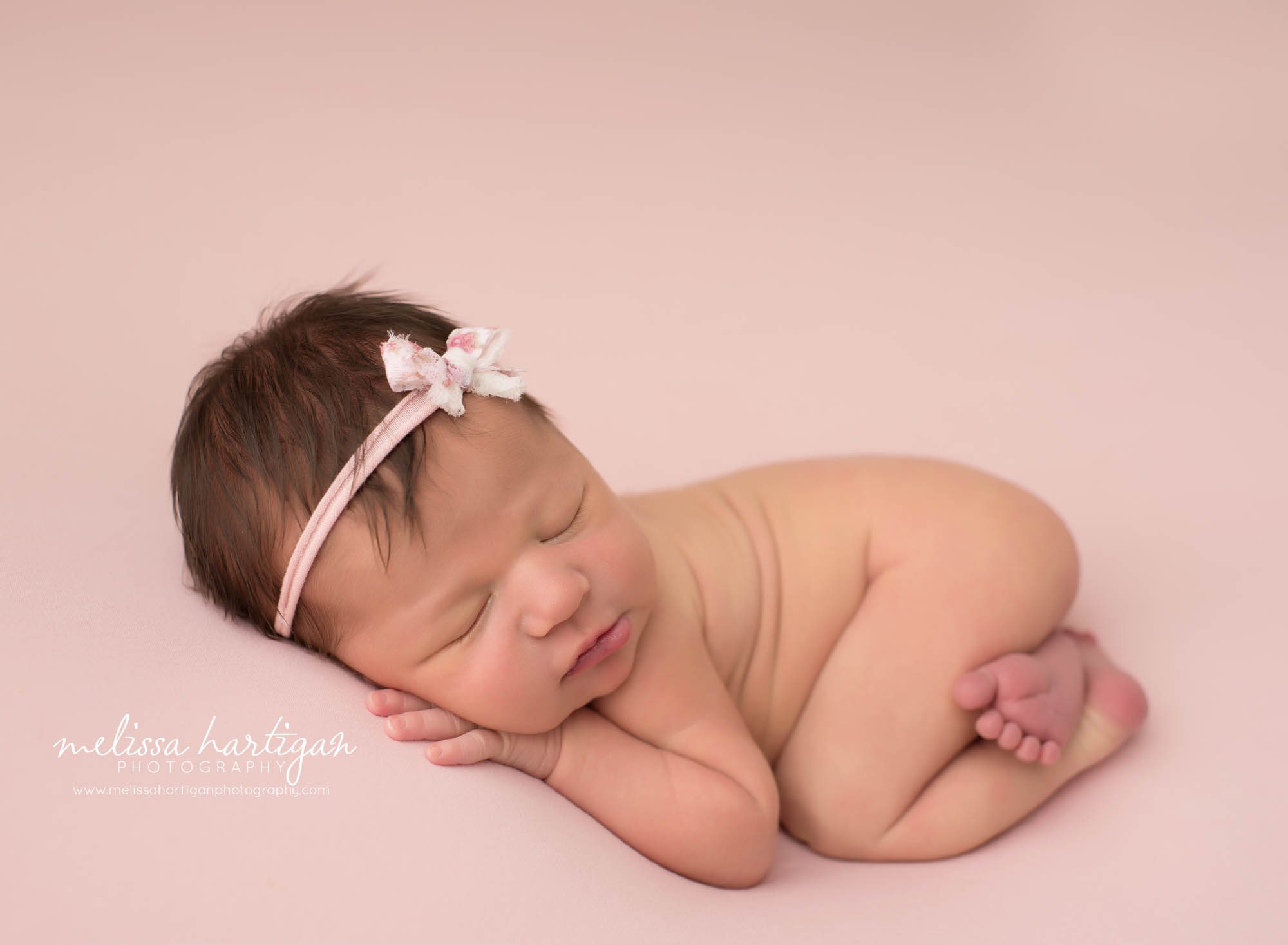 newborn baby girl posed on side bump up with pink bow headband