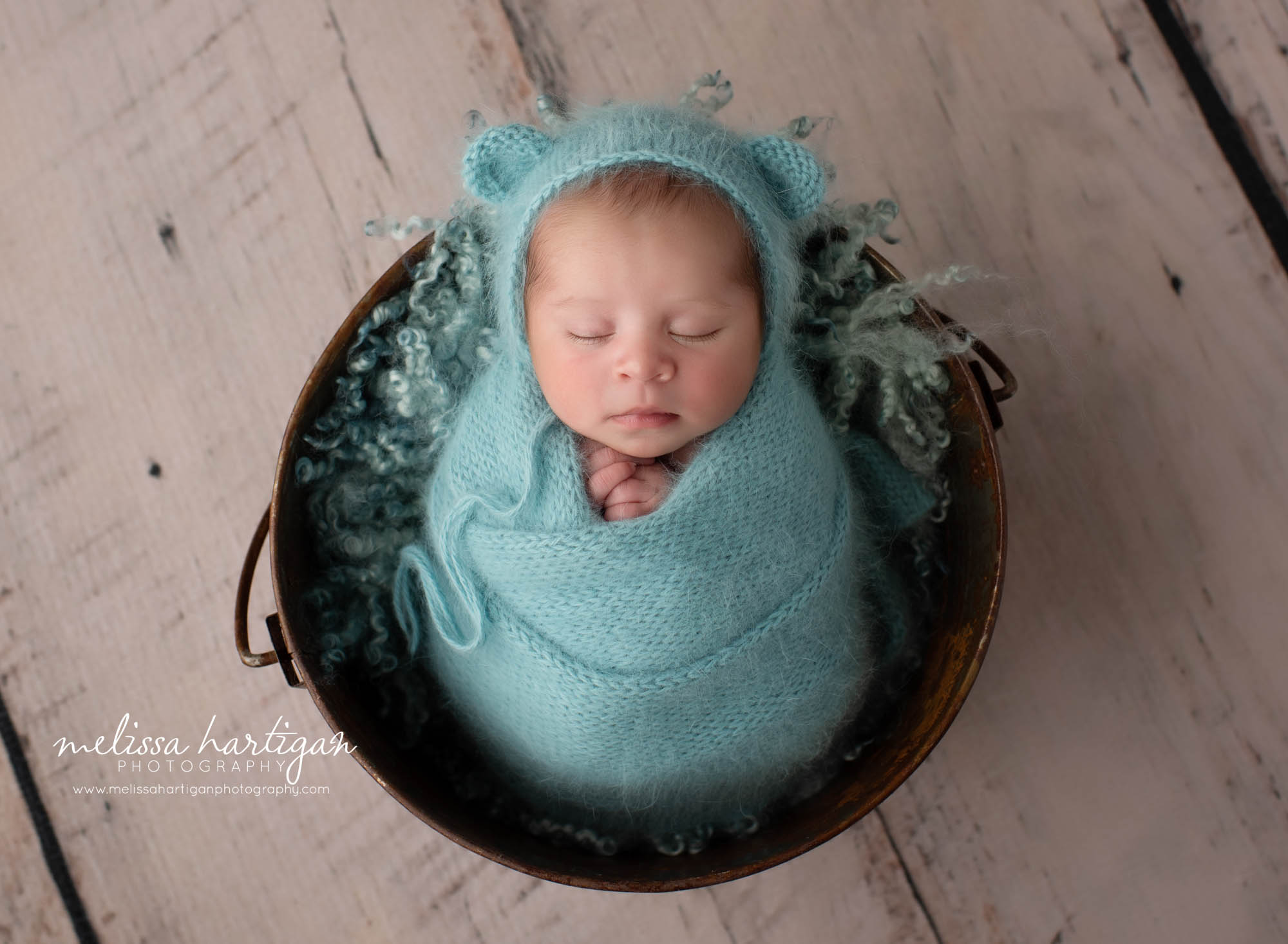 Newborn baby boy wrapped in teal colored knitted wrap with matching bear bonnet posed in bucket Newborn Photographer CT