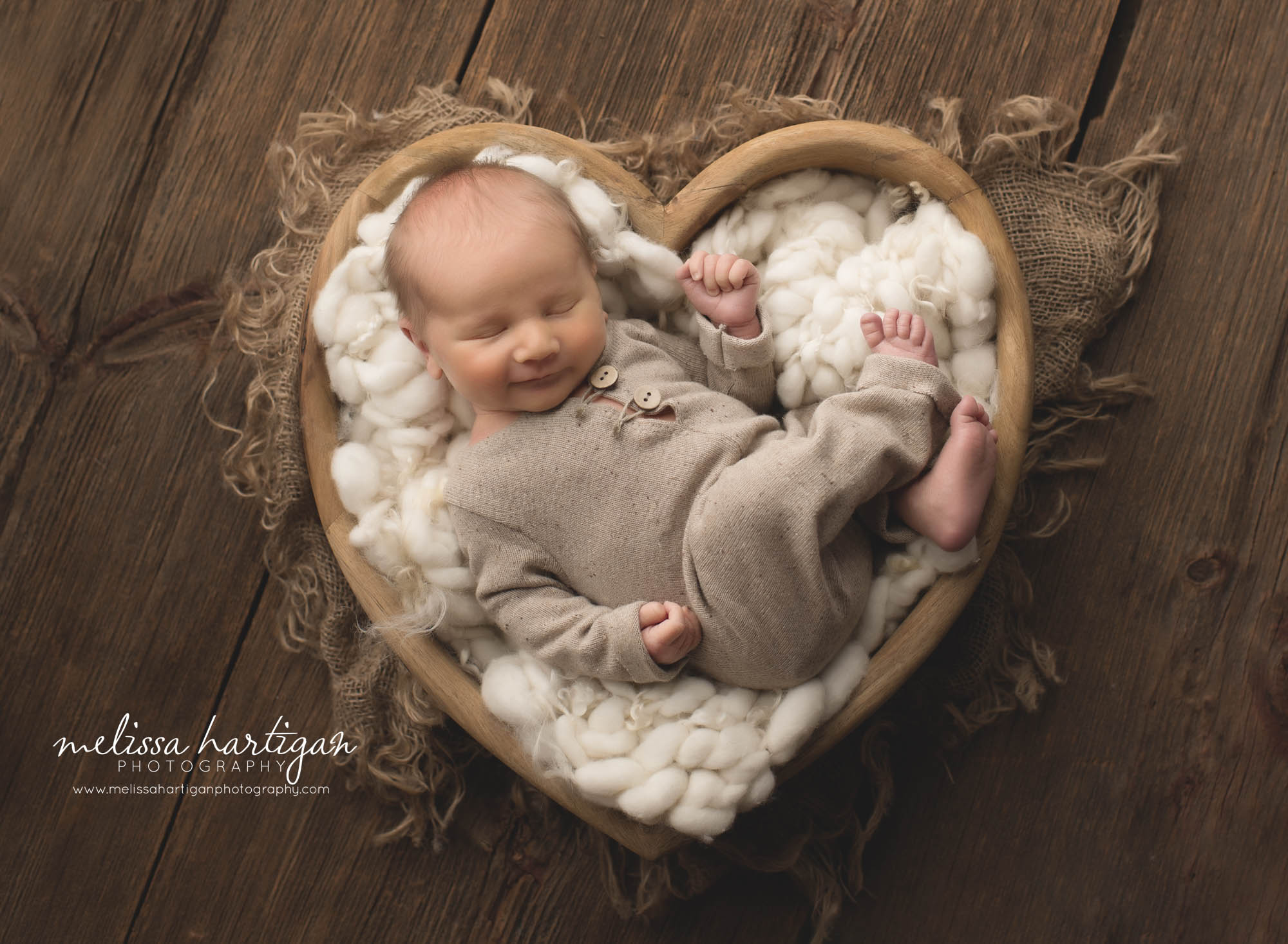 newborn baby boy posed in wooden heart shaped prop with cream fluffy layer and burlap layer under prop