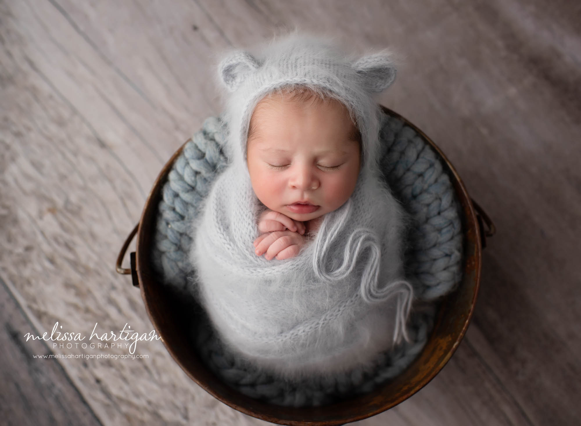 Newborn baby boy wrapped in knitted gray wrap with matching bear bonnet