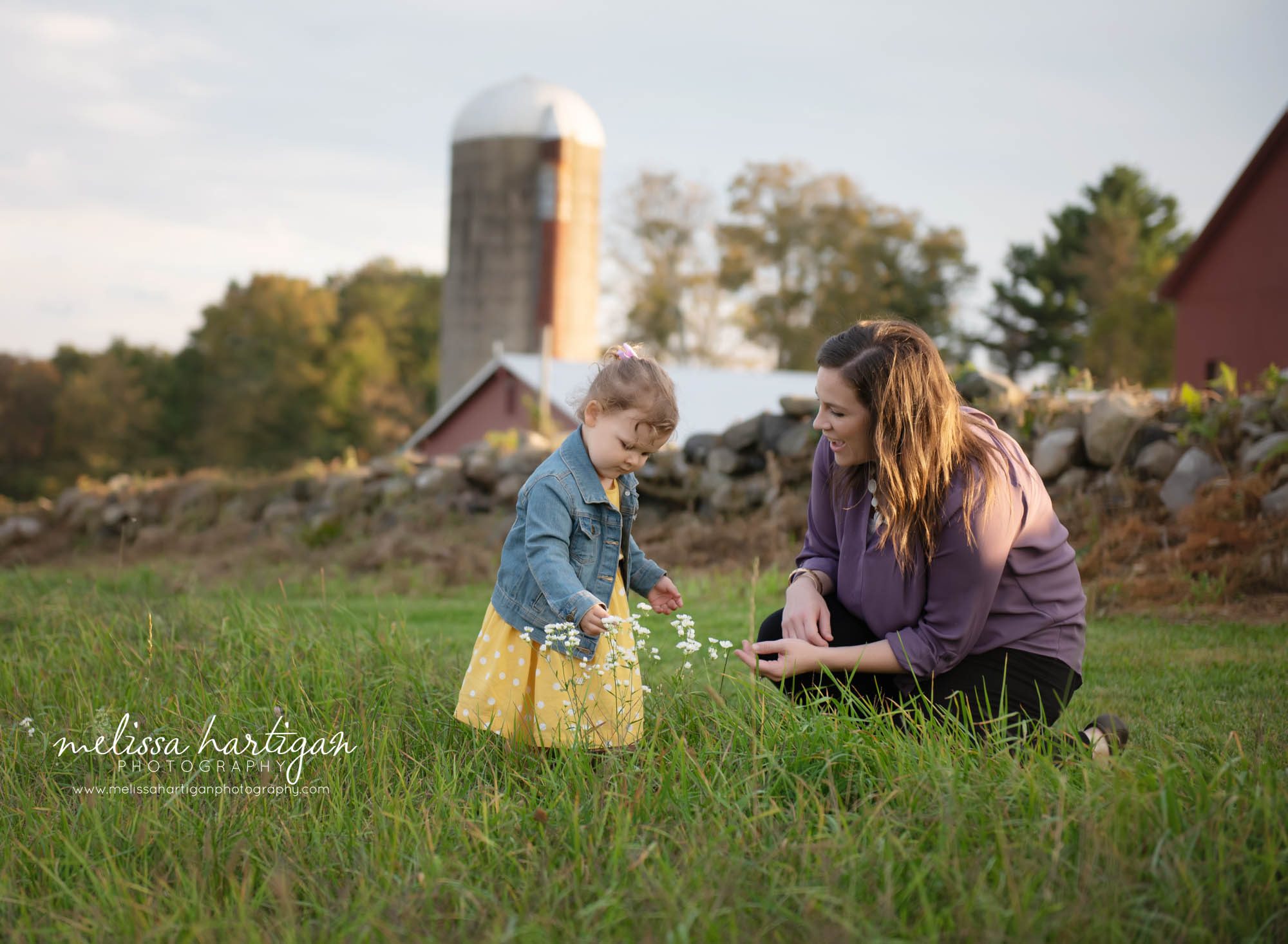 mom kneeling down with toddler daughter picking flowers in field family photography session