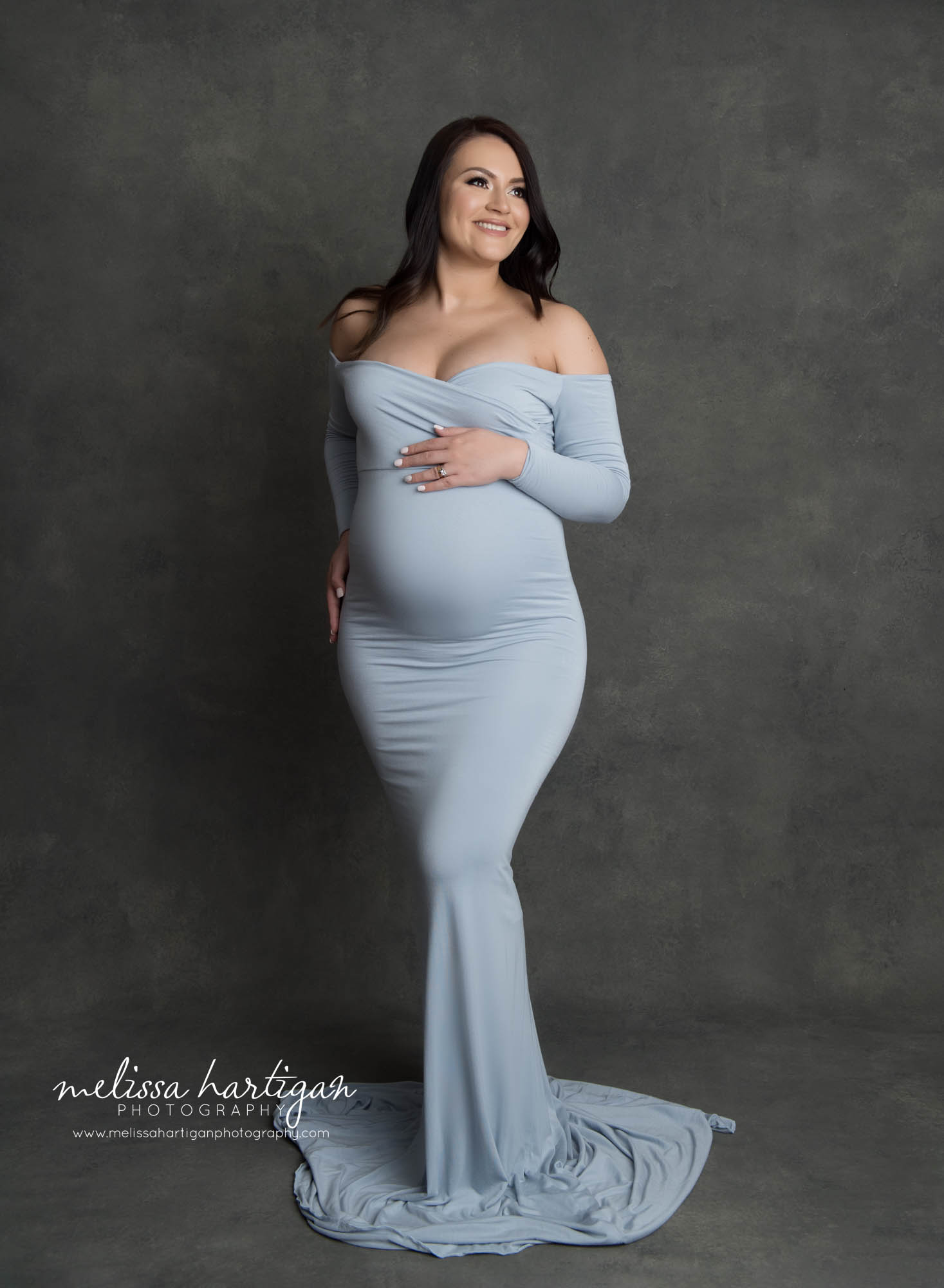 pregnant mom smiling off to side wearing long blue form fitting maternity dress