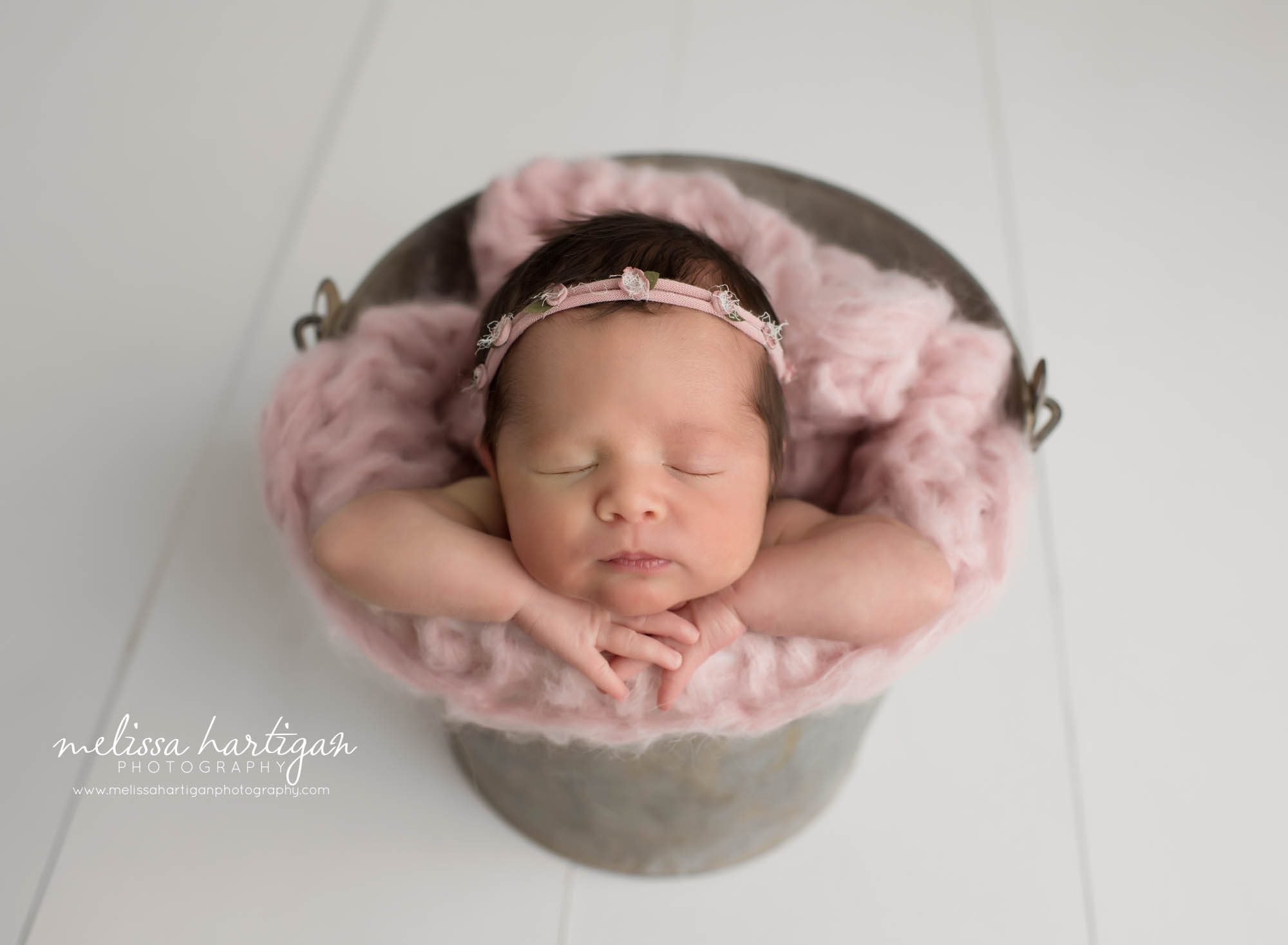 newborn baby girl posed in bucket wearing pink headband with tiny pink rosebuds