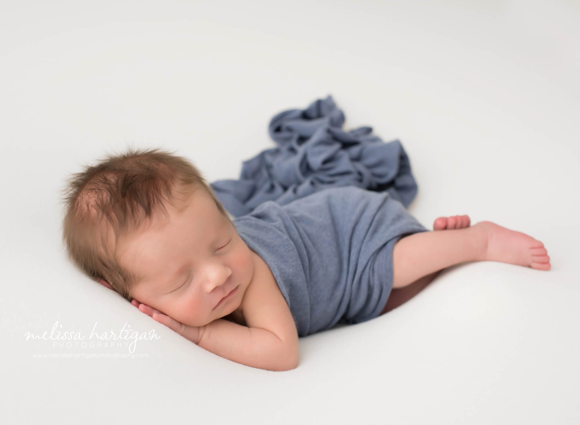 baby boy posed on side with blue wrap draped over him with hand tucked under chin