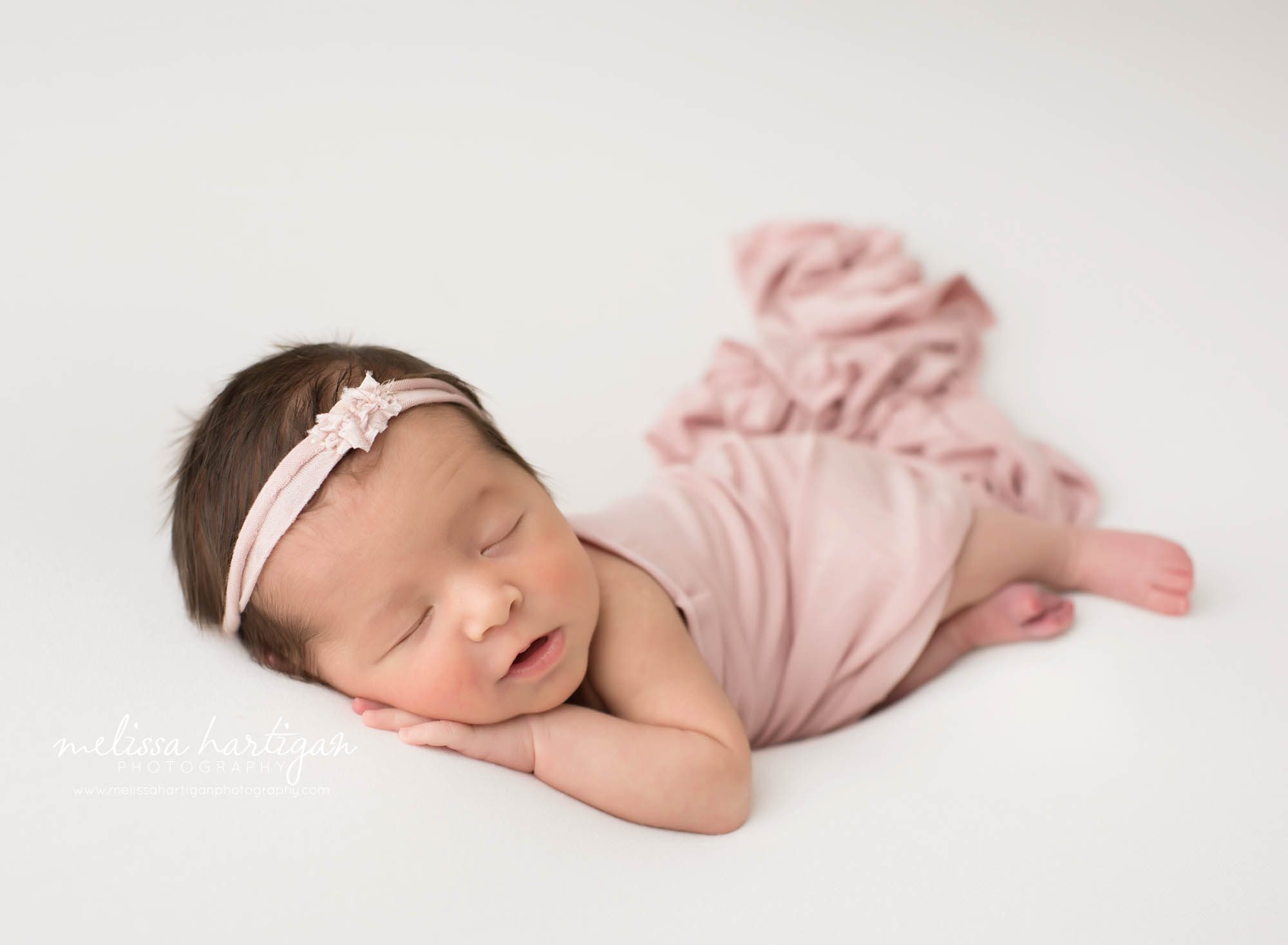 newborn baby girl posed on side with pink headband and pink wrap drapped over