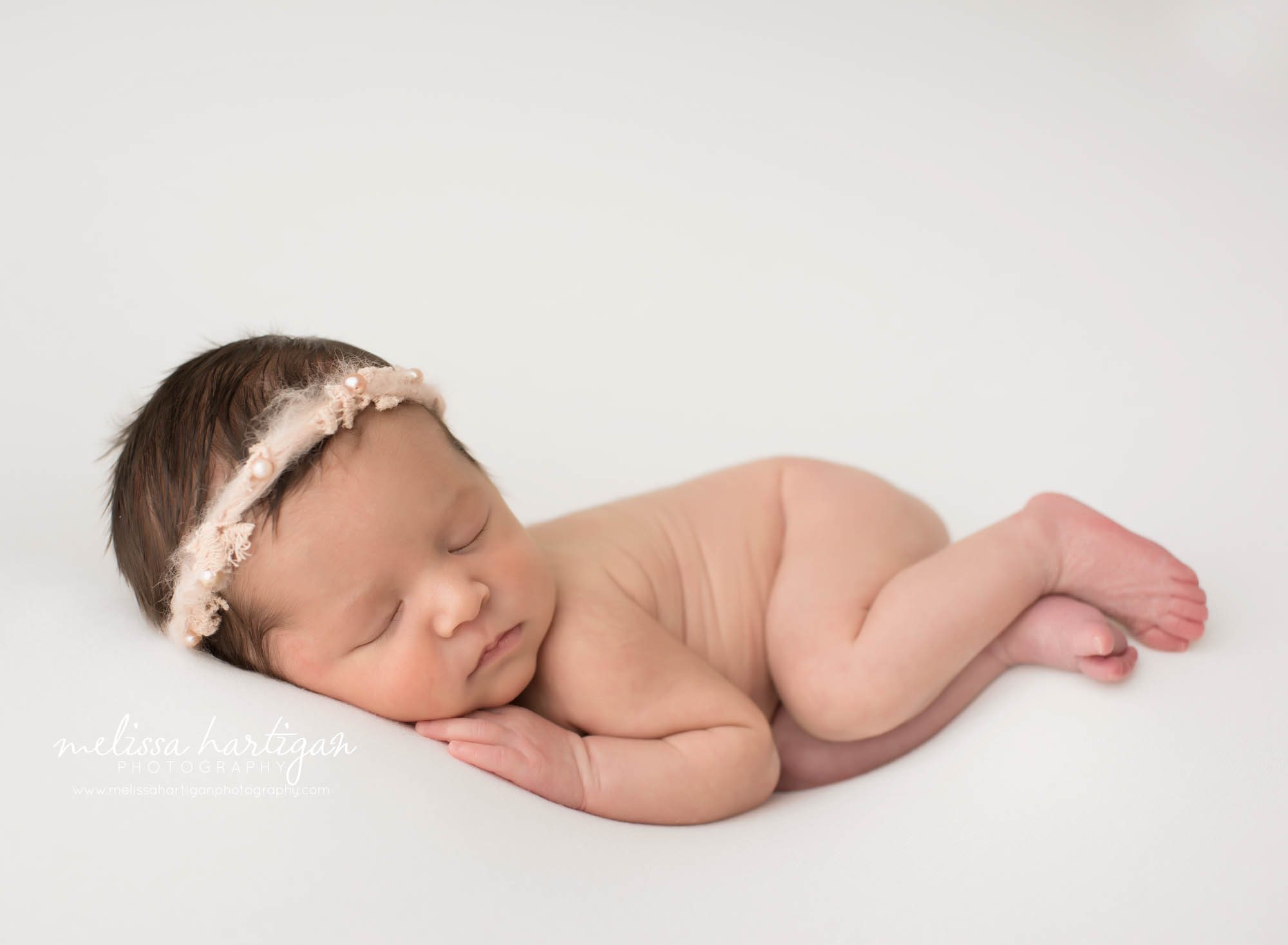 Newborn baby girl posed on side with pink halo headband