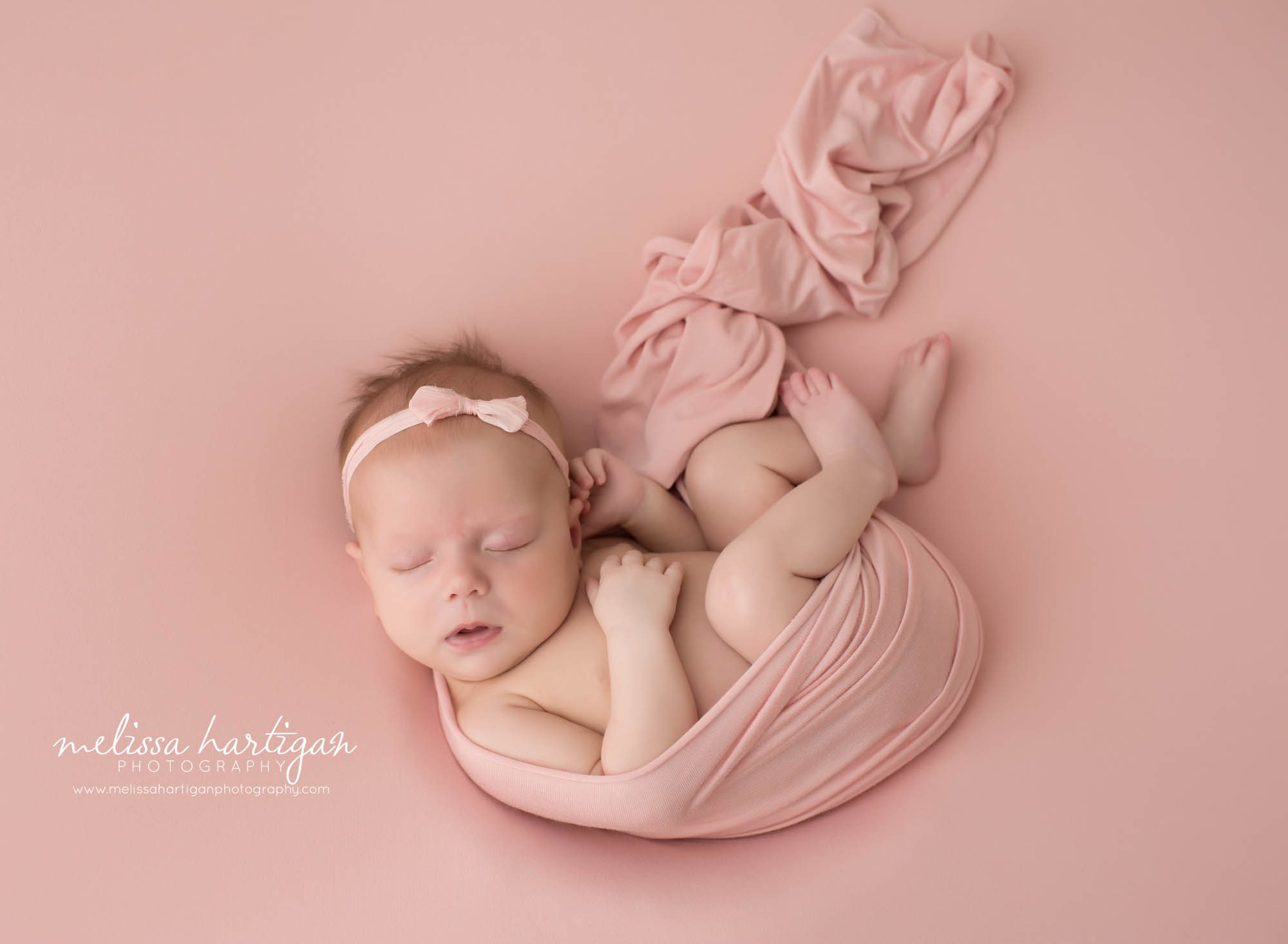 newborn baby girl posed on pink backdrop with pink wrap beautifully posed best CT newborn photography CT