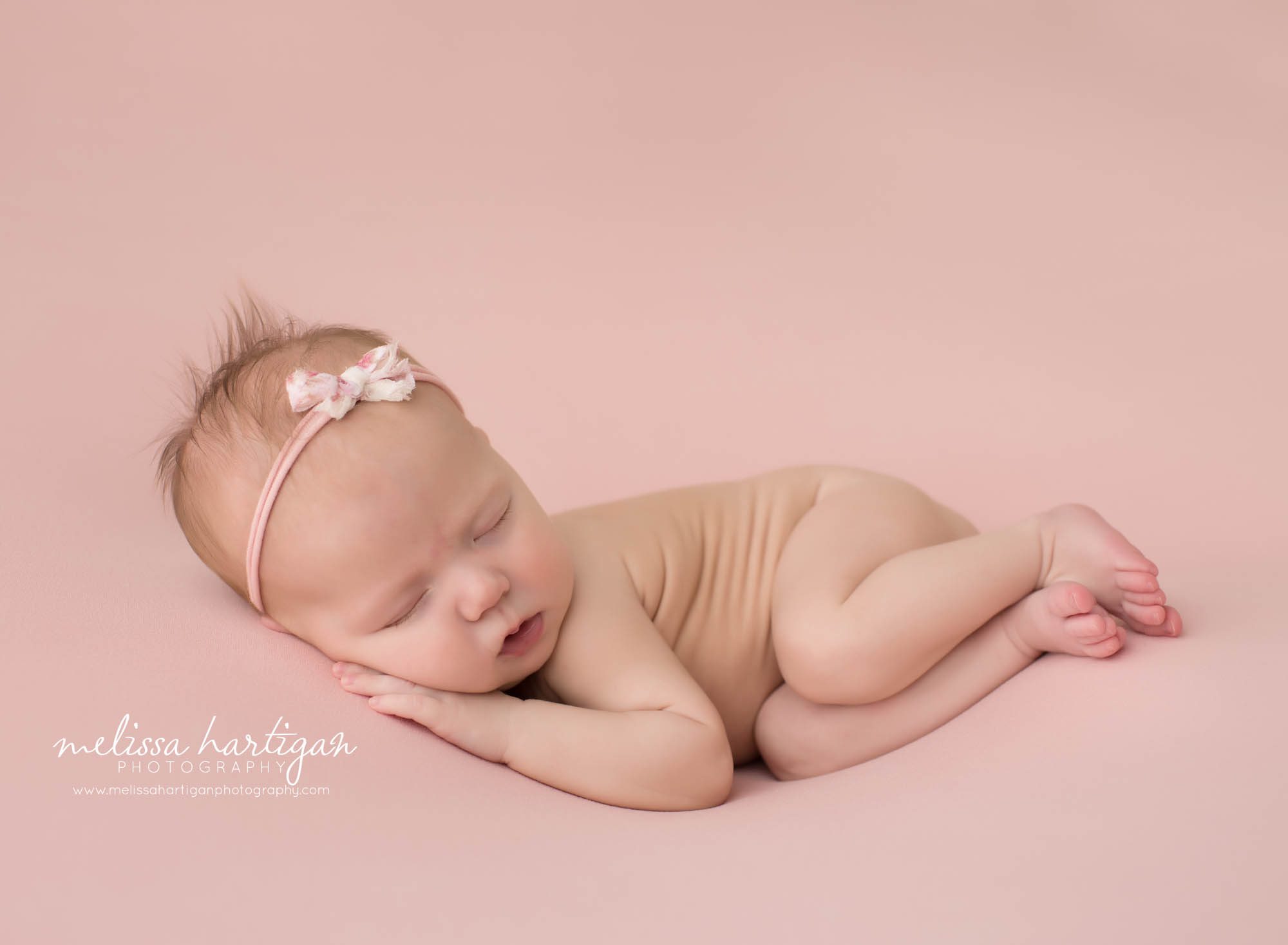 newborn baby girl posed on side on pink backdrop with bow headband