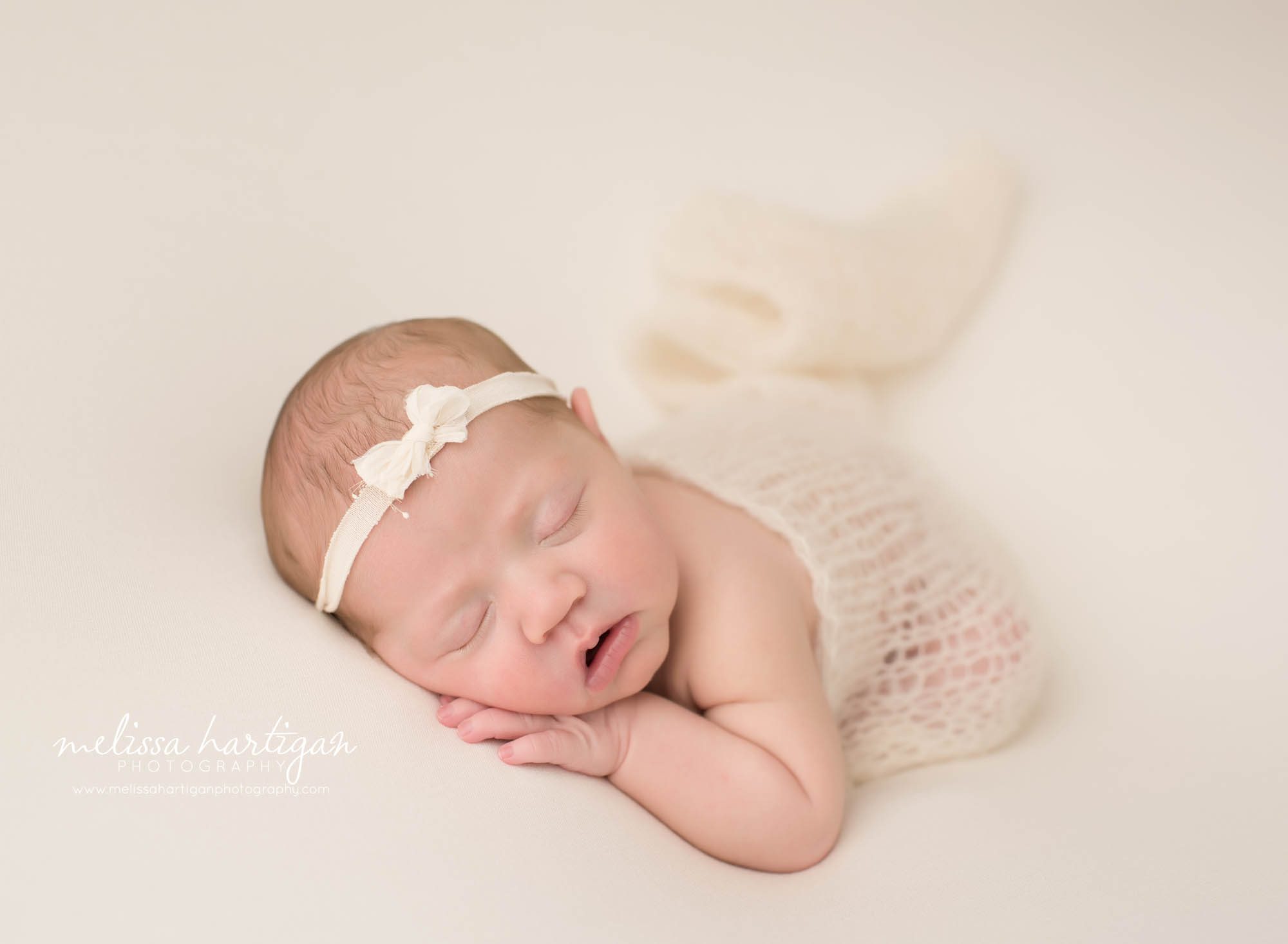 newborn baby girl posed on side with cream knit wrap and cream bow headband