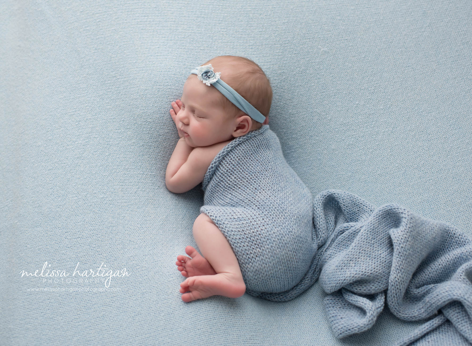 Baby girl posed on side with blue knitted wrap draped over baby
