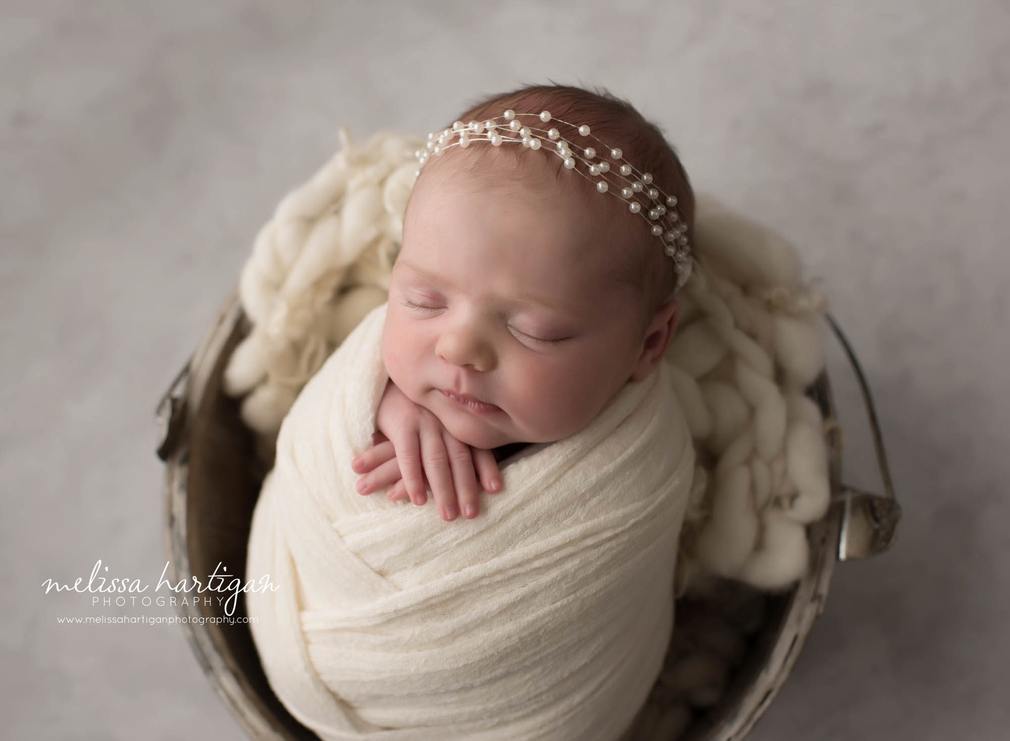 Newborn baby girl posed in metal bucket wrapped in cream wrap with beaded headband