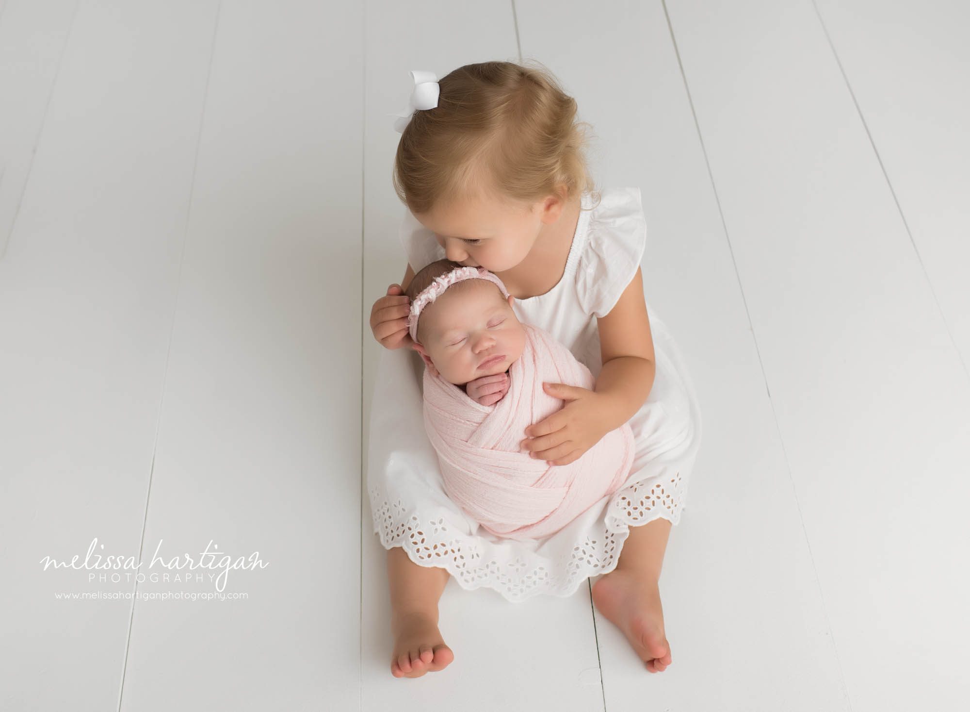 little sister kissing newborn baby sister on head