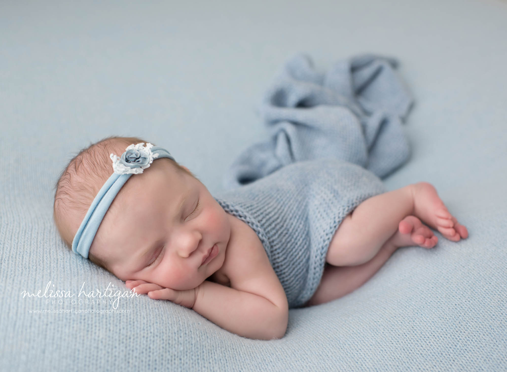 Newborn baby girl posed on side with hand under chin blue knitted wrap draped over baby Ct newborn Photography studio session