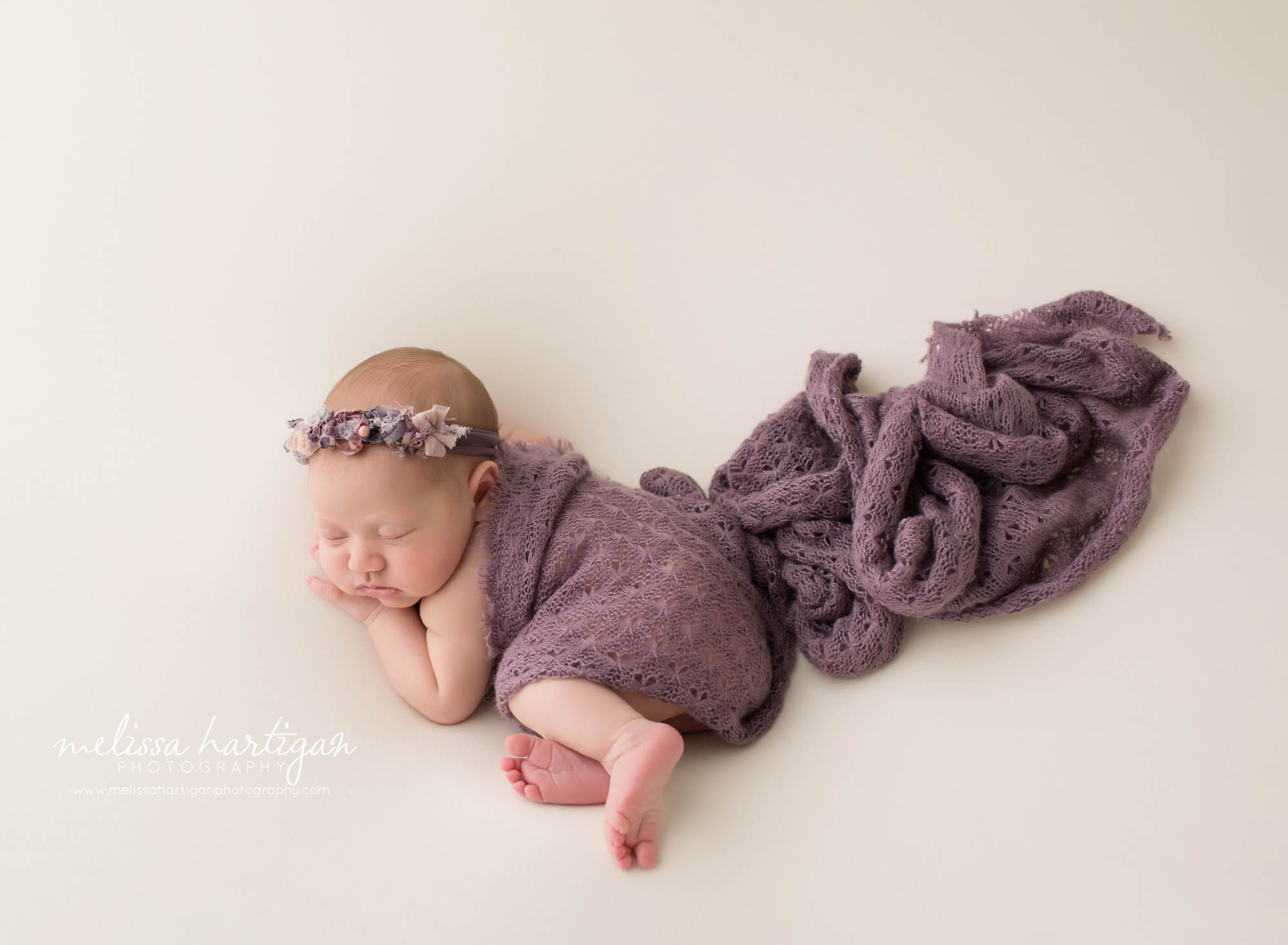 newborn baby girl posed on side with purple layer wrap draped over and purple headband