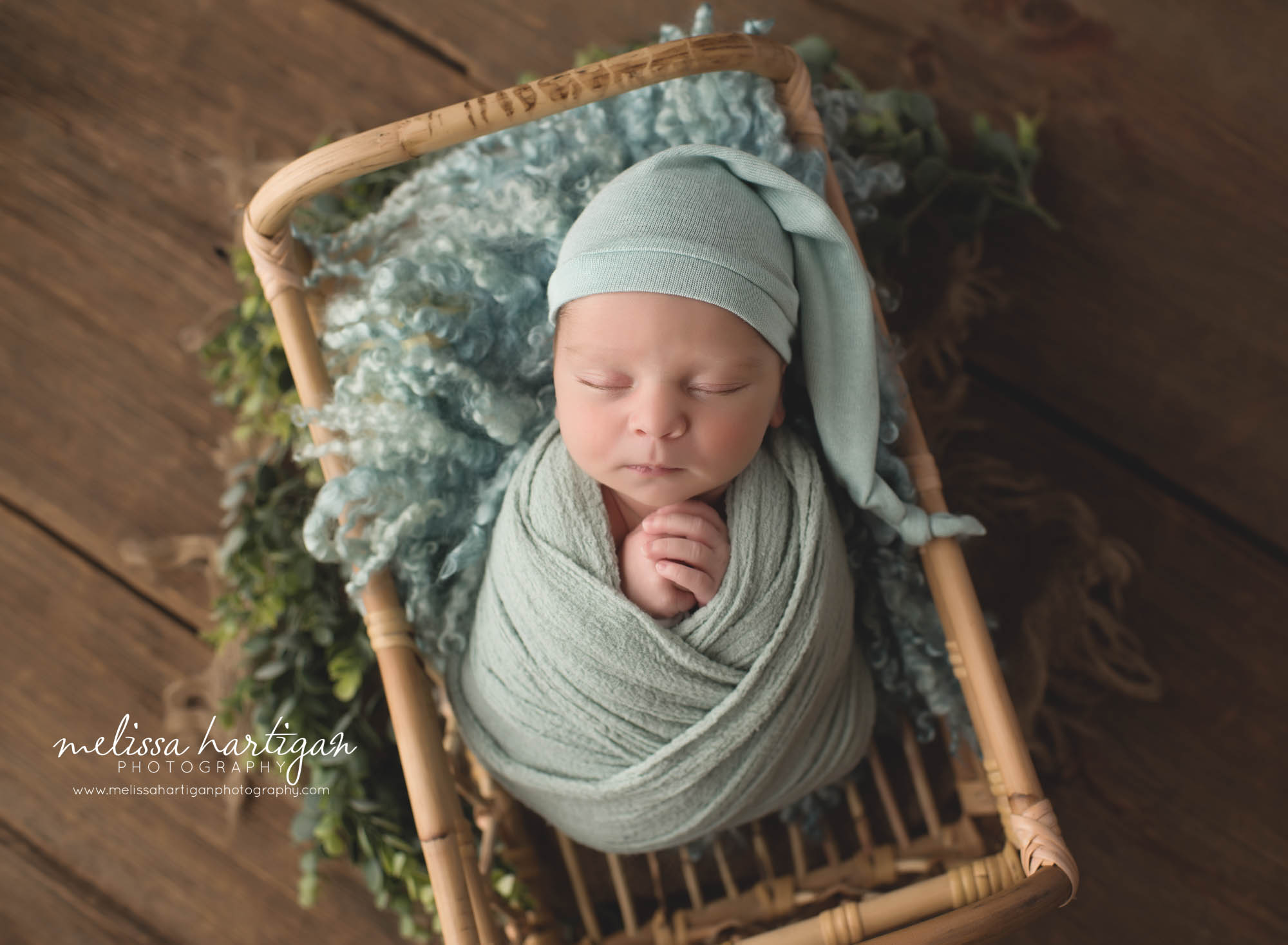 newborn baby boy posed in basket with mint green sleepy cap and wrap