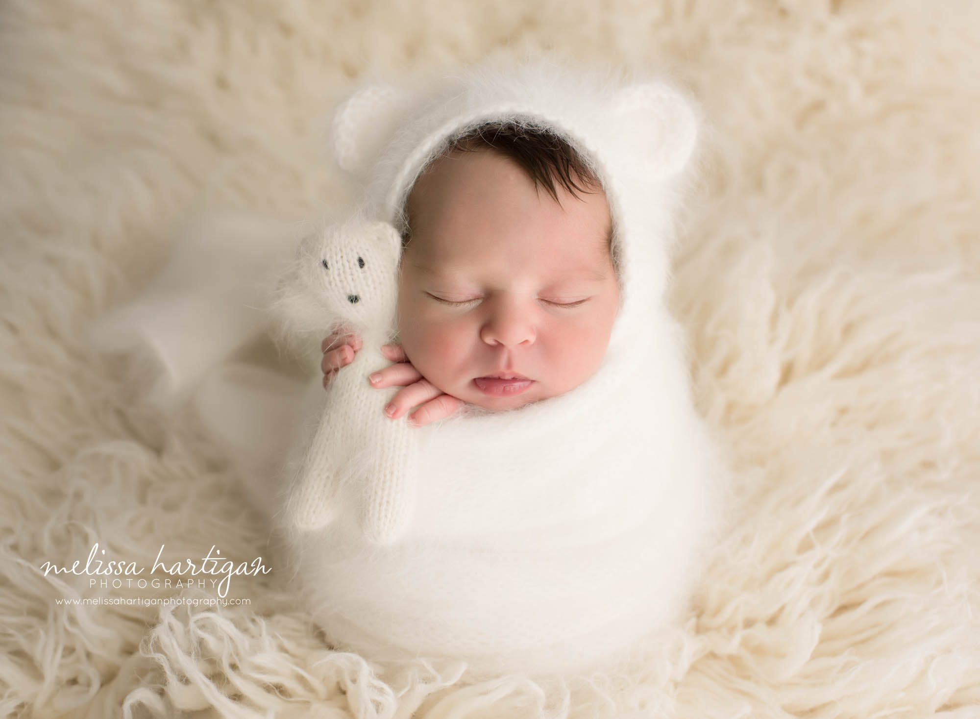 newborn baby boy wrapped in white knitted layer wrap with matching bear bonnet and teddy bear