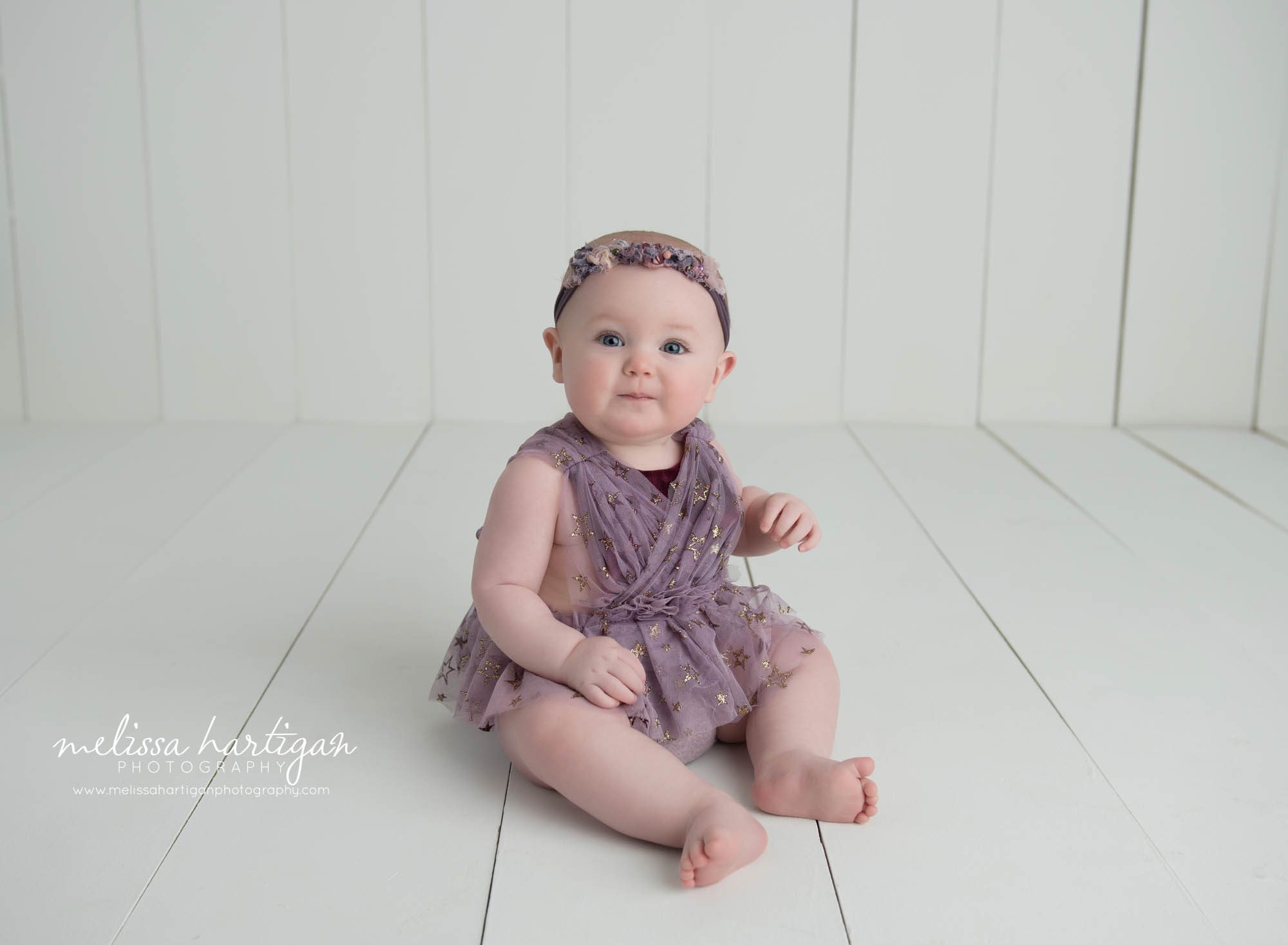 baby girl sitting on studio wooden boards wearing gold star purple outfit with purple headband Baby photographer CT